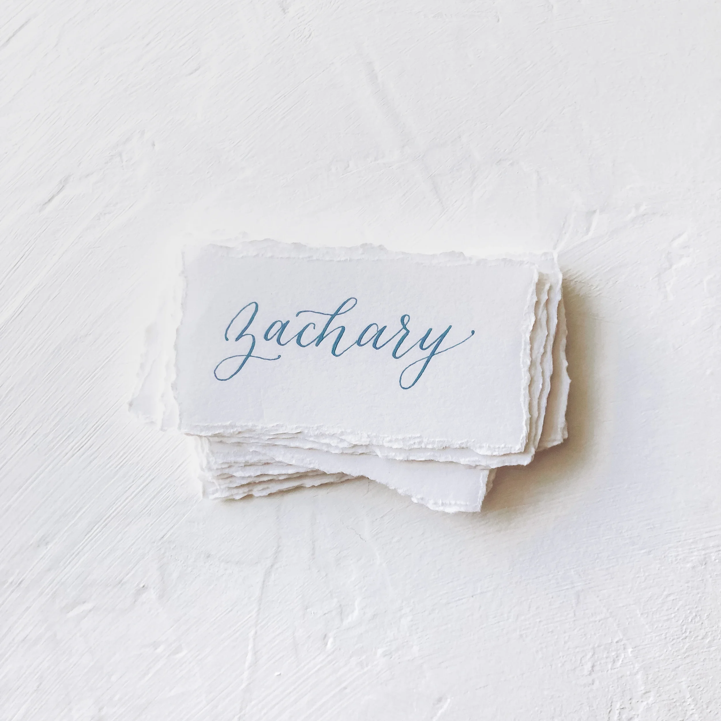 Stack of torn edge place cards with dusty blue calligraphy ink.