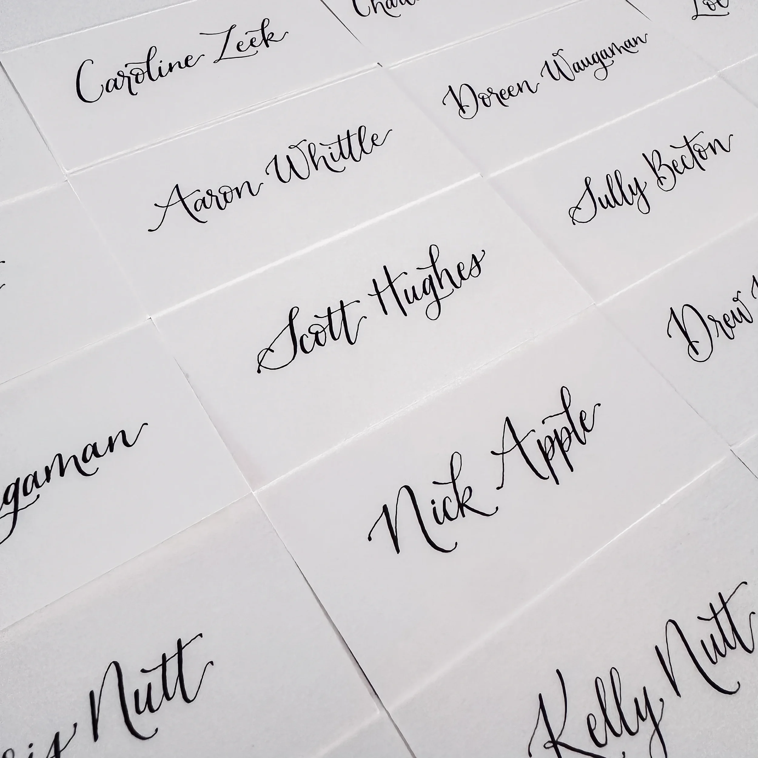 Embrace the timeless elegance of minimalist day-of stationery with a classic white folded place card. Showcasing clean, high-contrast black script calligraphy, this simple paper name card rests beautifully on natural wood or formal linen settings for