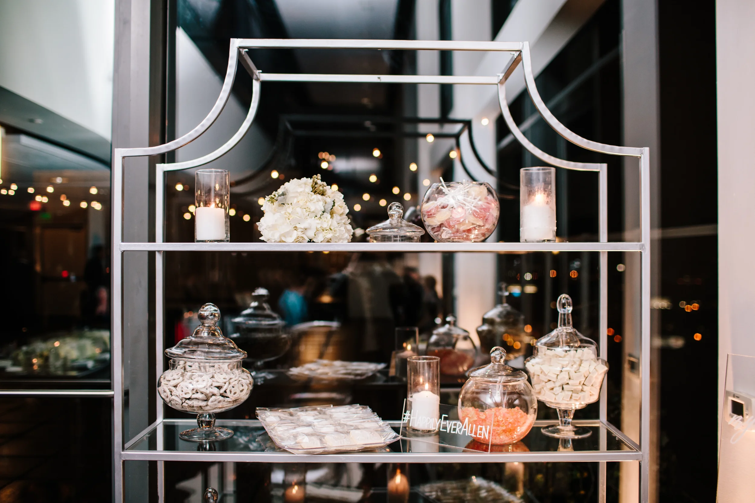 Personalize your modern ceremony or entryway with custom clear acrylic wedding hashtag signage. This design is hand-painted in white ink, adding an elegant sentiment to a contemporary metropolitan wedding venue.