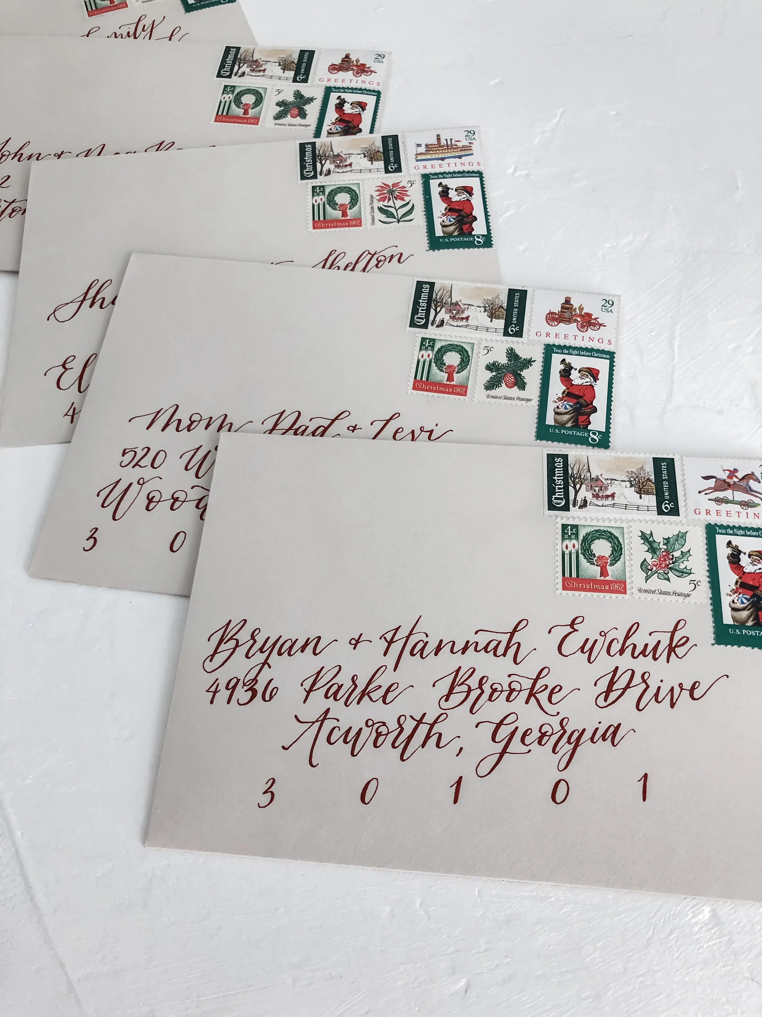 Taupe kraft paper envelopes addressed in a deep burgundy calligraphy font with vintage Christmas stamps for Christmas cards.