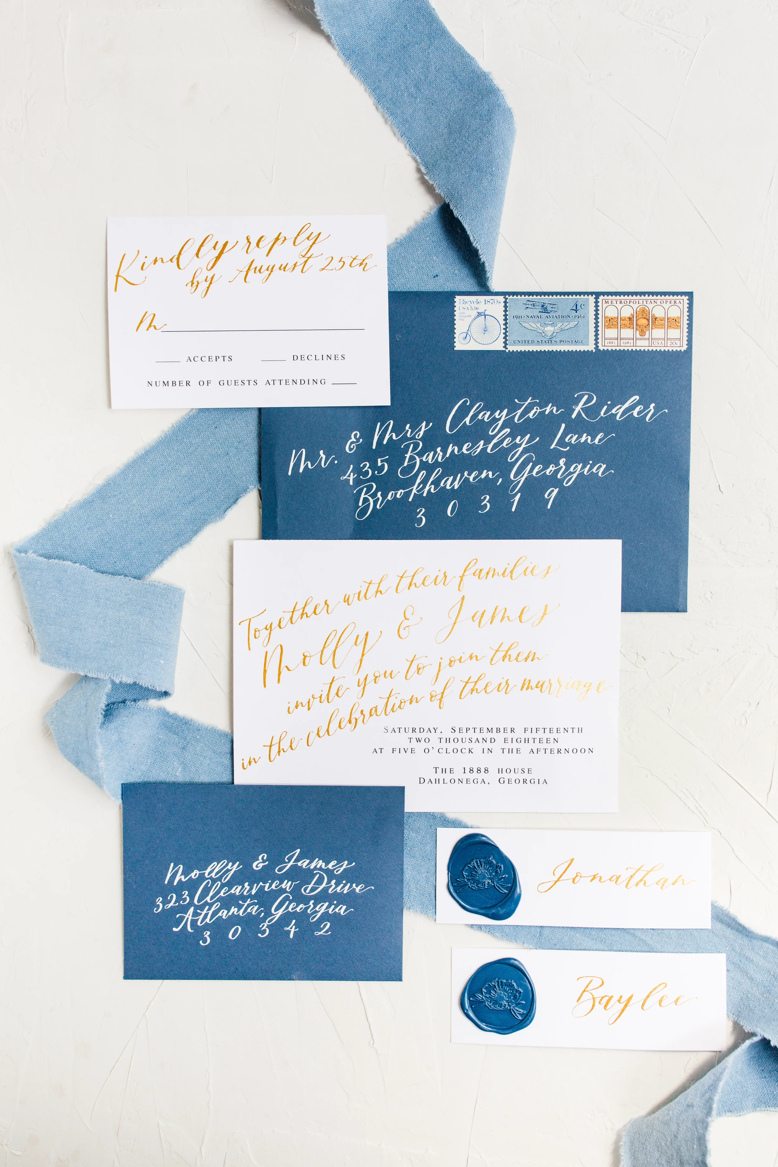 Dusty blue and white wedding invitation suite flat lay with gold metallic calligraphy script and blue silk ribbon.