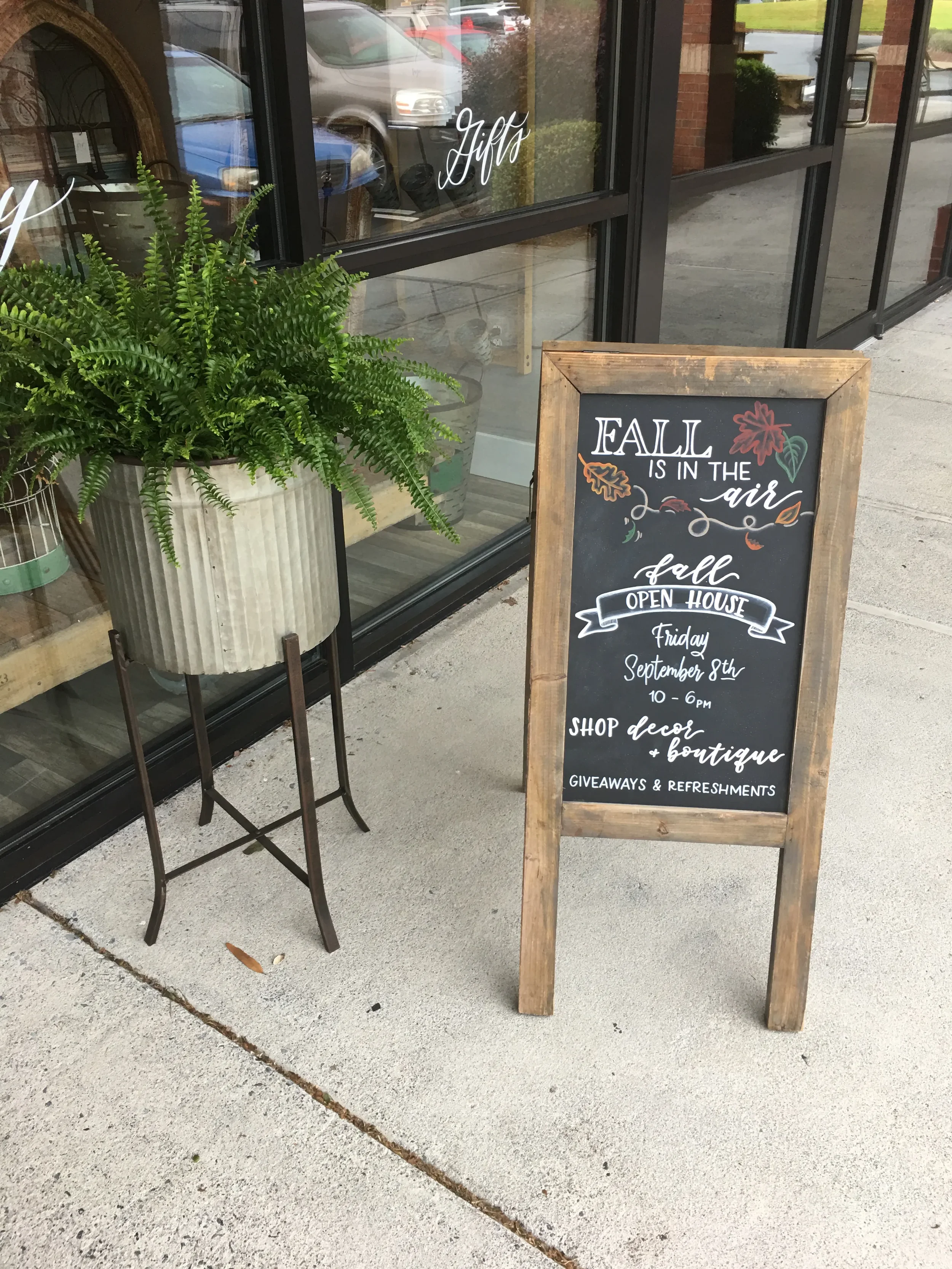 Autumn sidewalk sandwich board sign with colorful chalk illustrations of pumpkins and falling leaves.