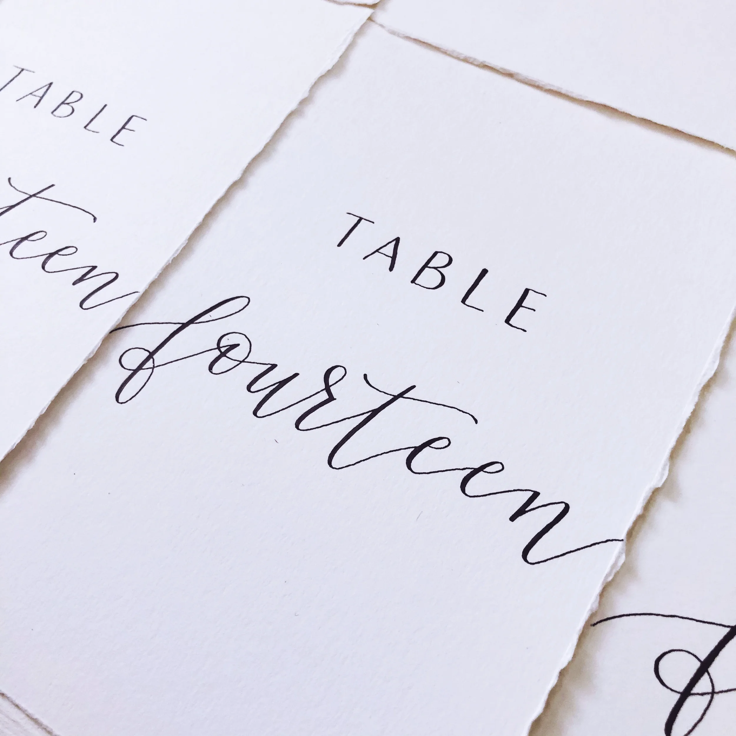 Classic white paper table number cards with fine-line cursive script in black ink.