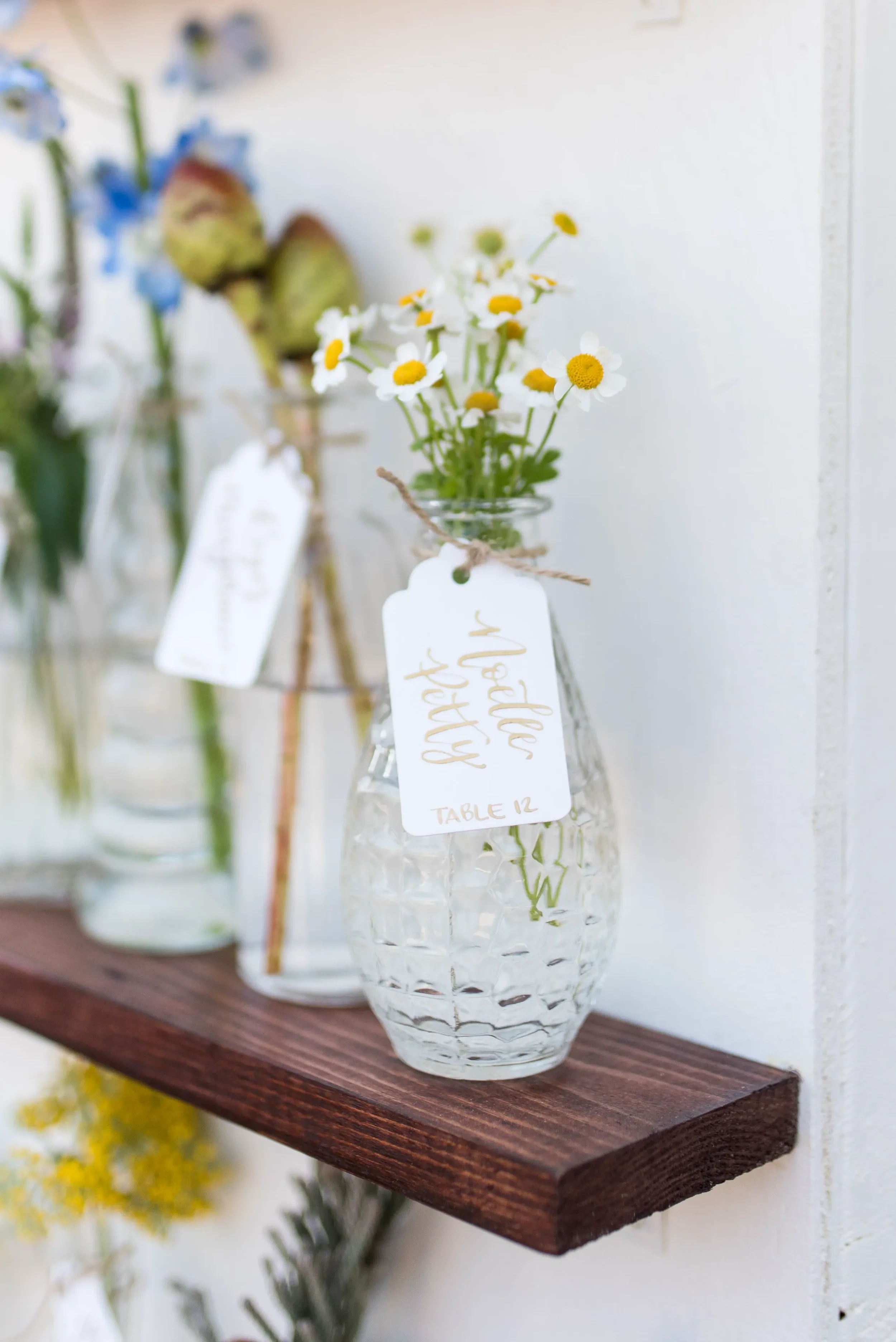 Whimsical garden wedding escort card display with clear glass bud vases and hand-lettered tags.