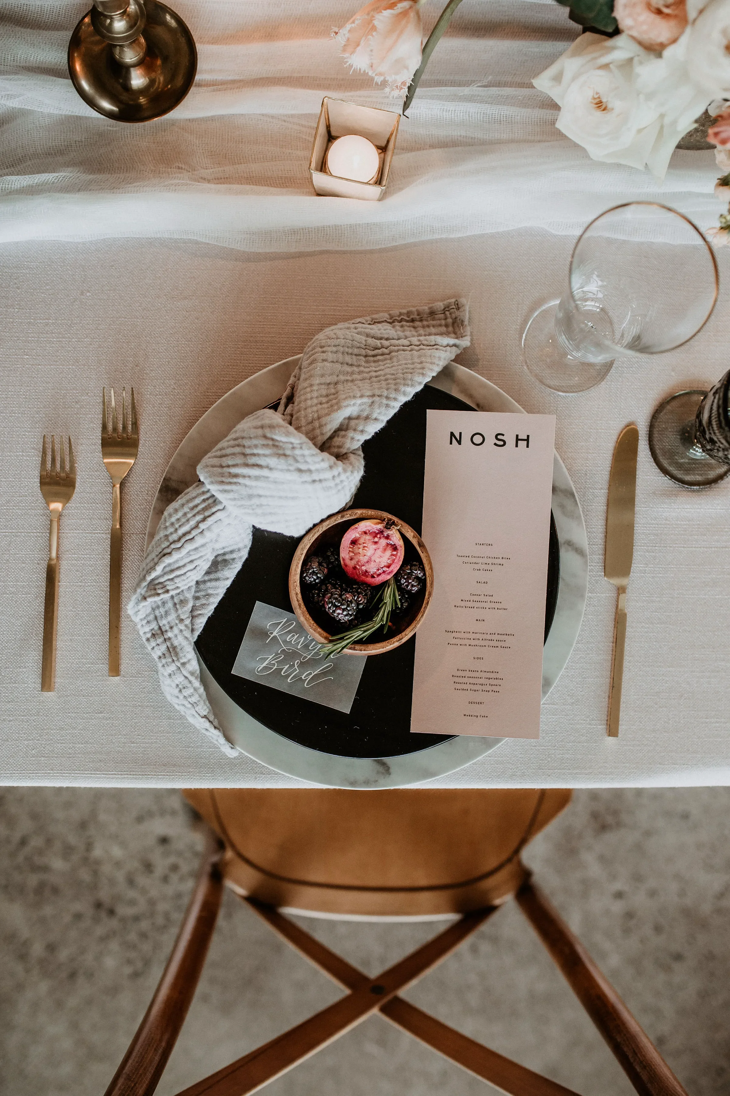 Translucent vellum place card with white script calligraphy resting on a modern blush dinner menu.