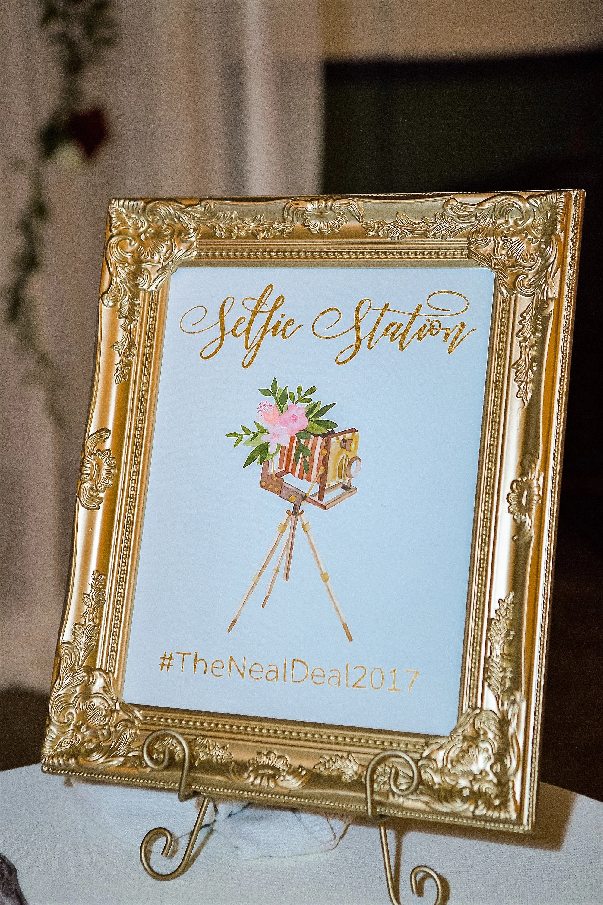 Vintage gold ornate frame displaying an illustrated watercolor "Selfie Station" sign with a custom wedding hashtag.