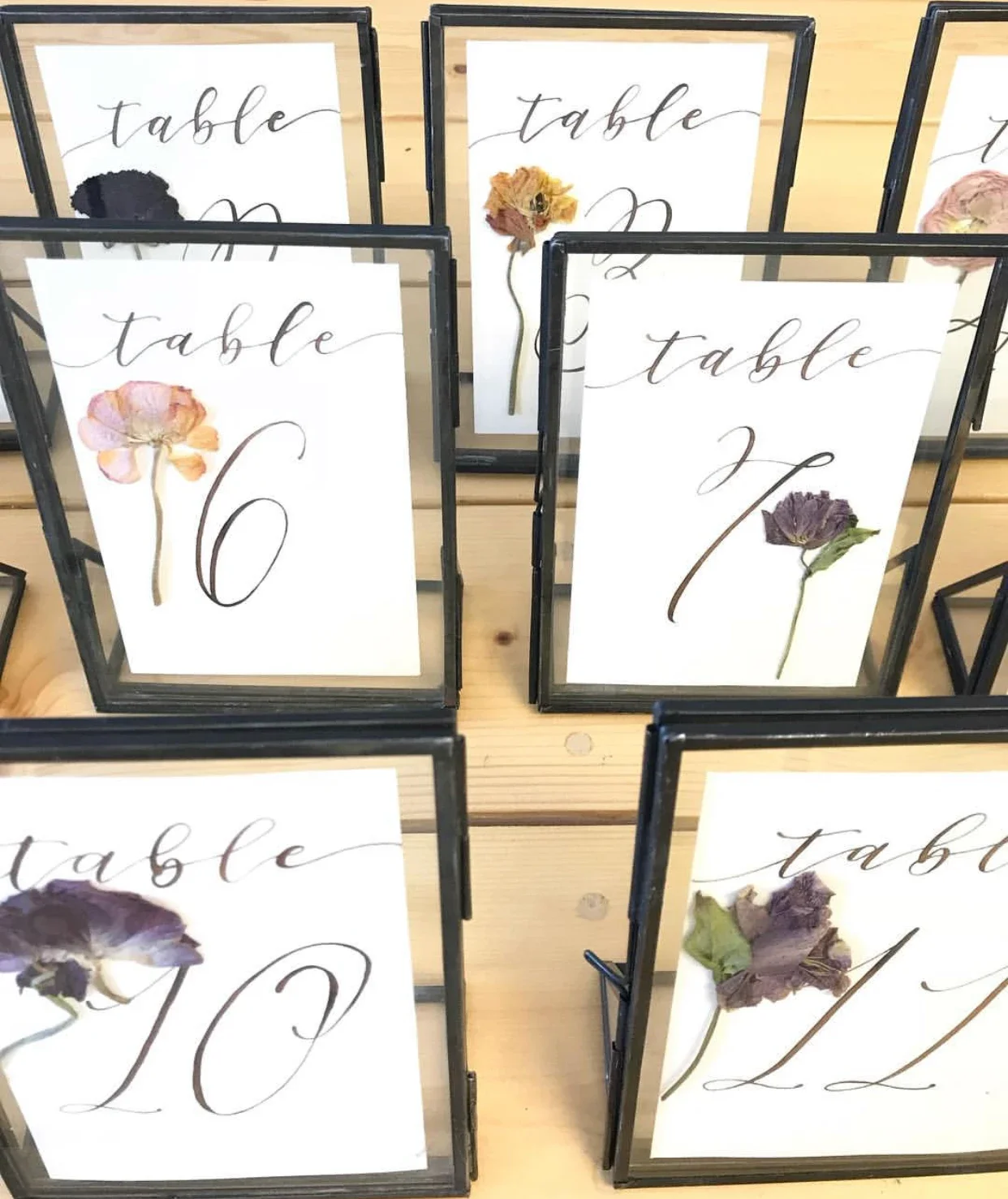 Bring delicate botanical elegance to your centerpieces with a pressed flower glass table number sign. Set in a double-glass frame with metallic gold hand-lettering, this piece anchors a romantic blush pink tablescape paired with lush garden roses in 