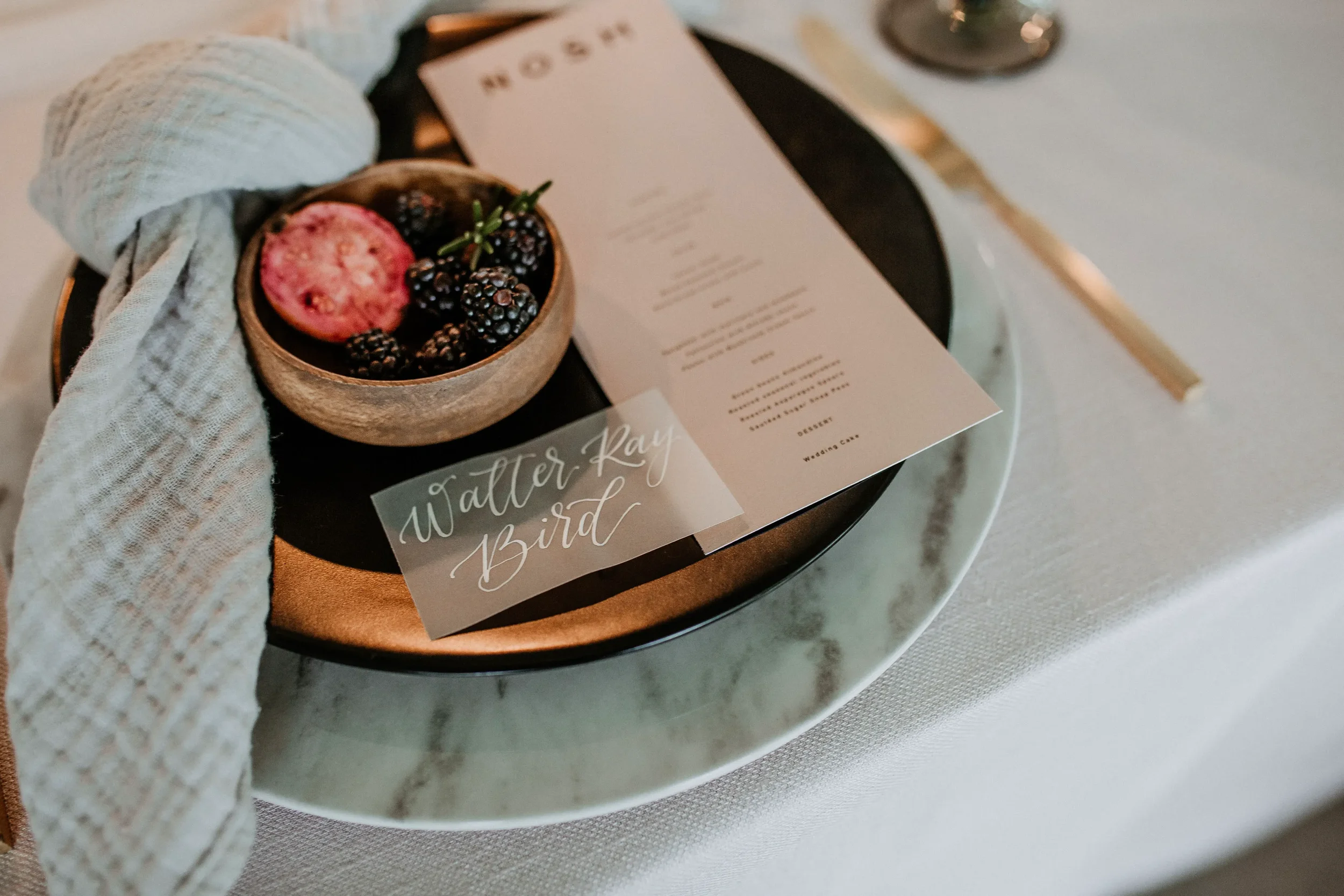 Translucent vellum place card with white script calligraphy resting on a modern blush dinner menu.