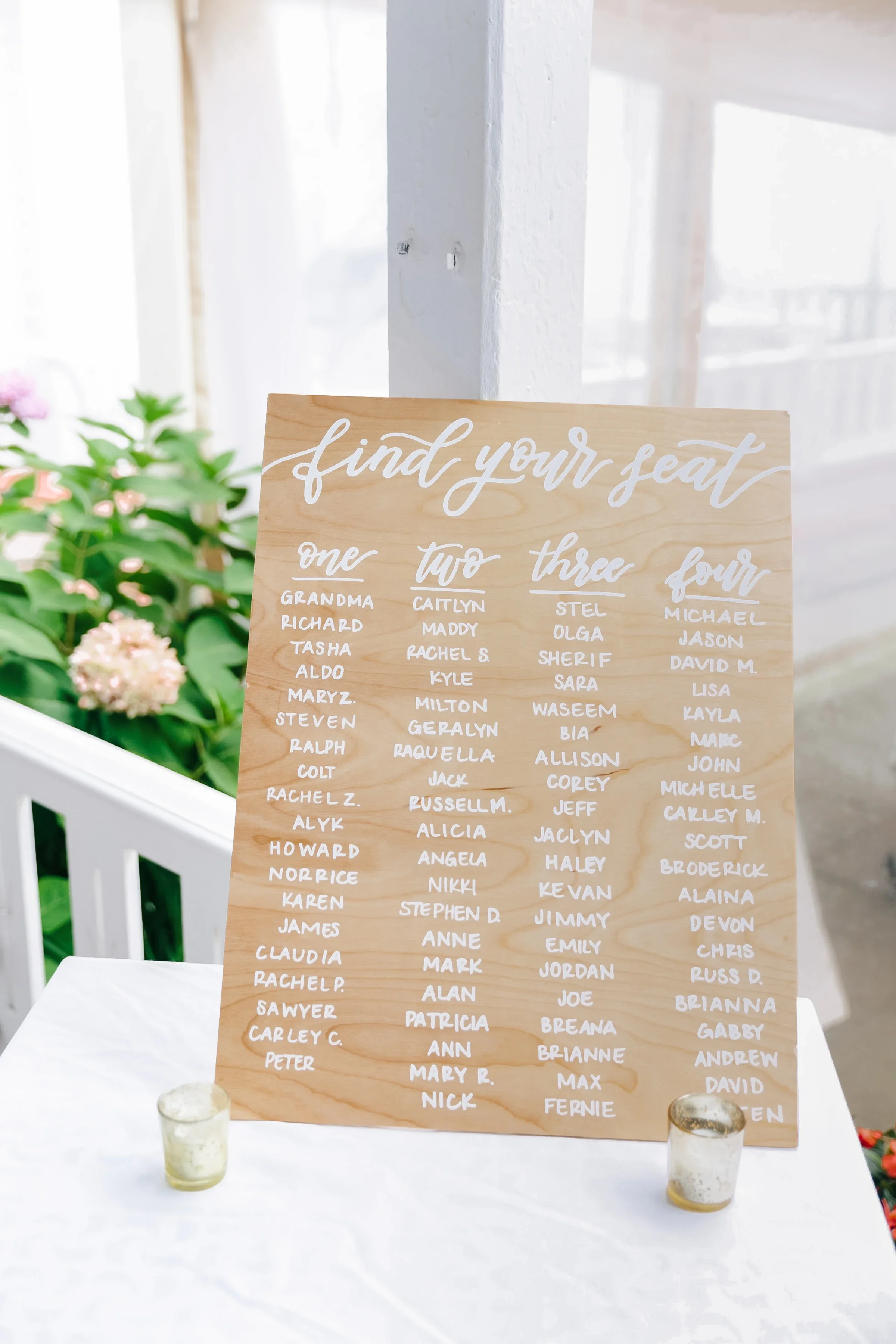 Vertical natural wood wedding seating board featuring four columns of guest names written in white script.