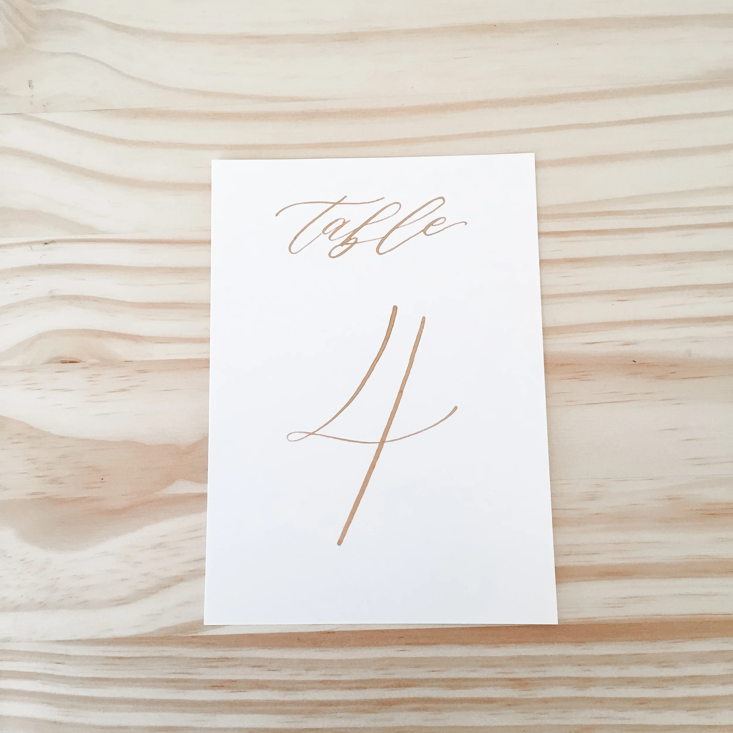 Gold calligraphy table numbers on white cardstock paper.