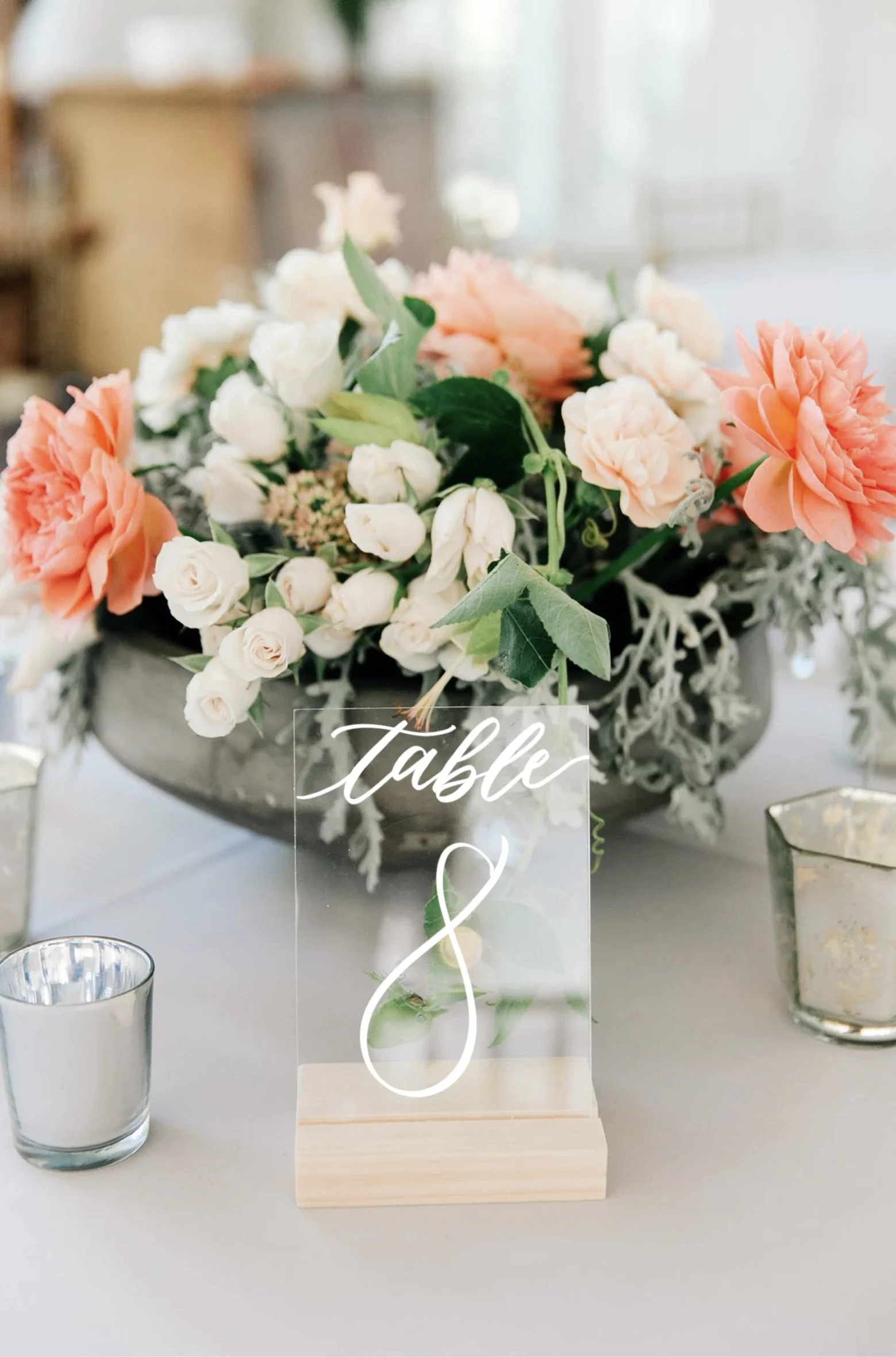 Freestanding clear acrylic table number with white script standing on a wooden block.