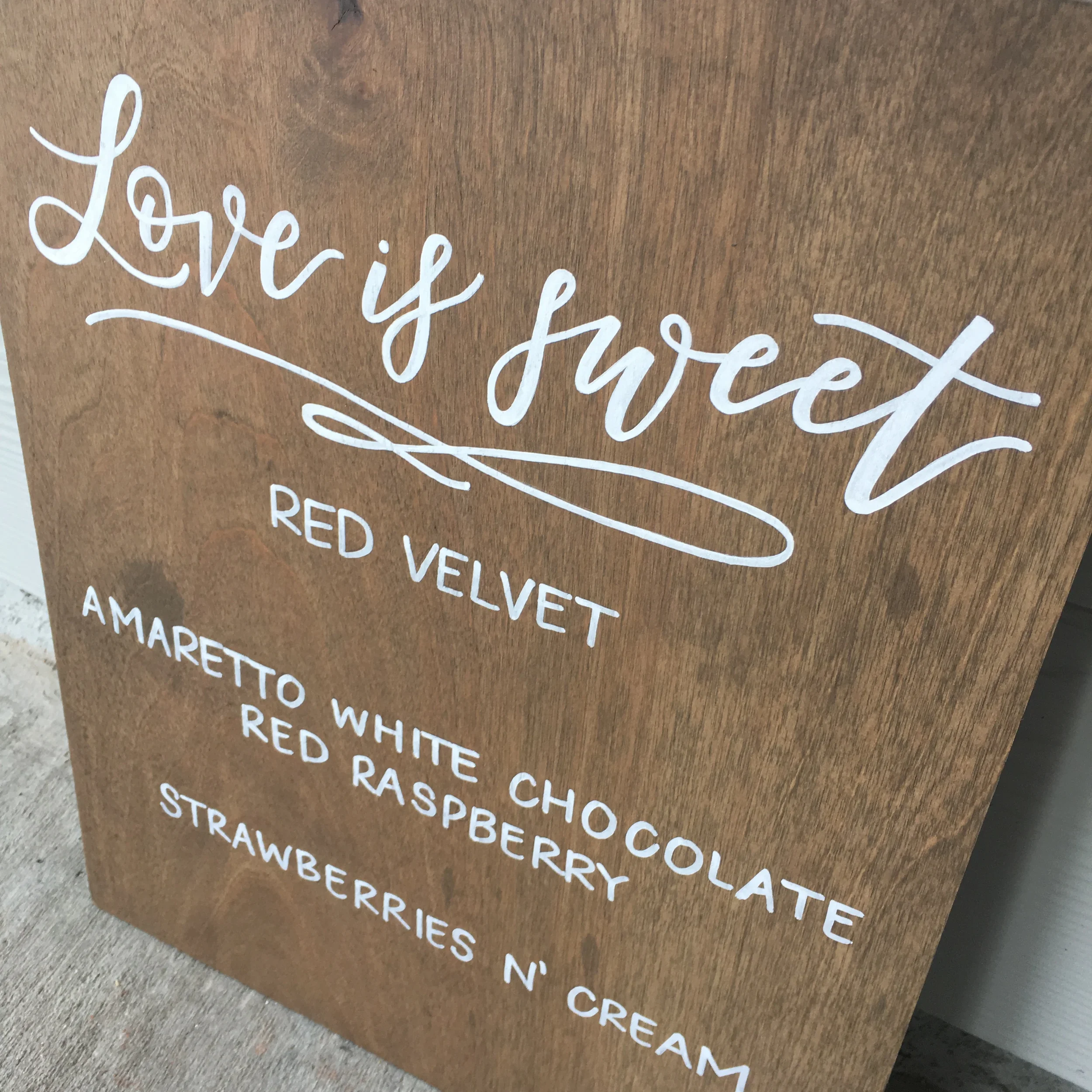 Hand-lettered wooden reception menu board displaying cake and cupcake flavor options in white ink.