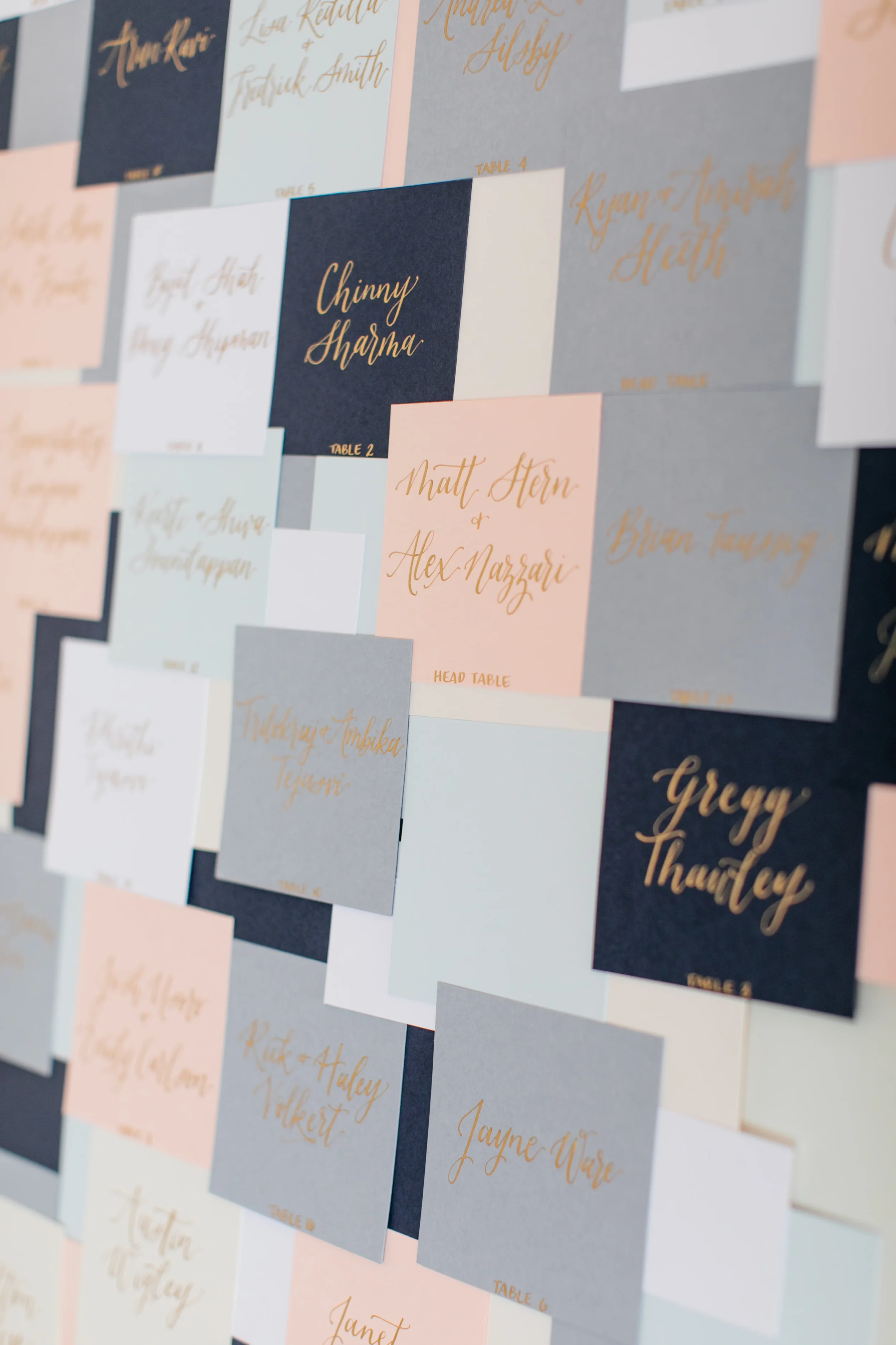 Color-blocked wedding escort card wall with shimmering copper and gold metallic calligraphy font.