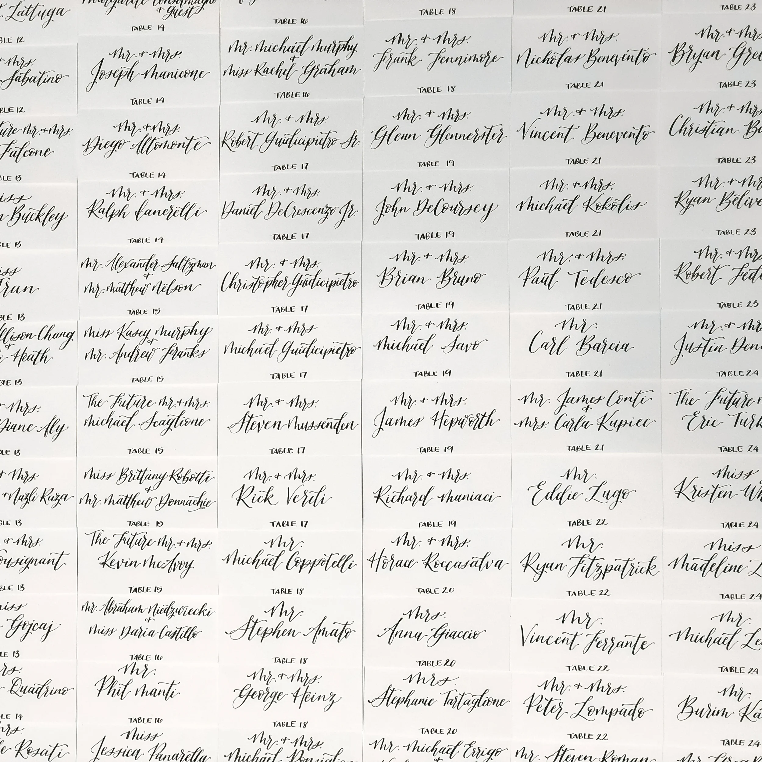 Large grid array of white folded wedding escort cards calligraphed in black script ink.