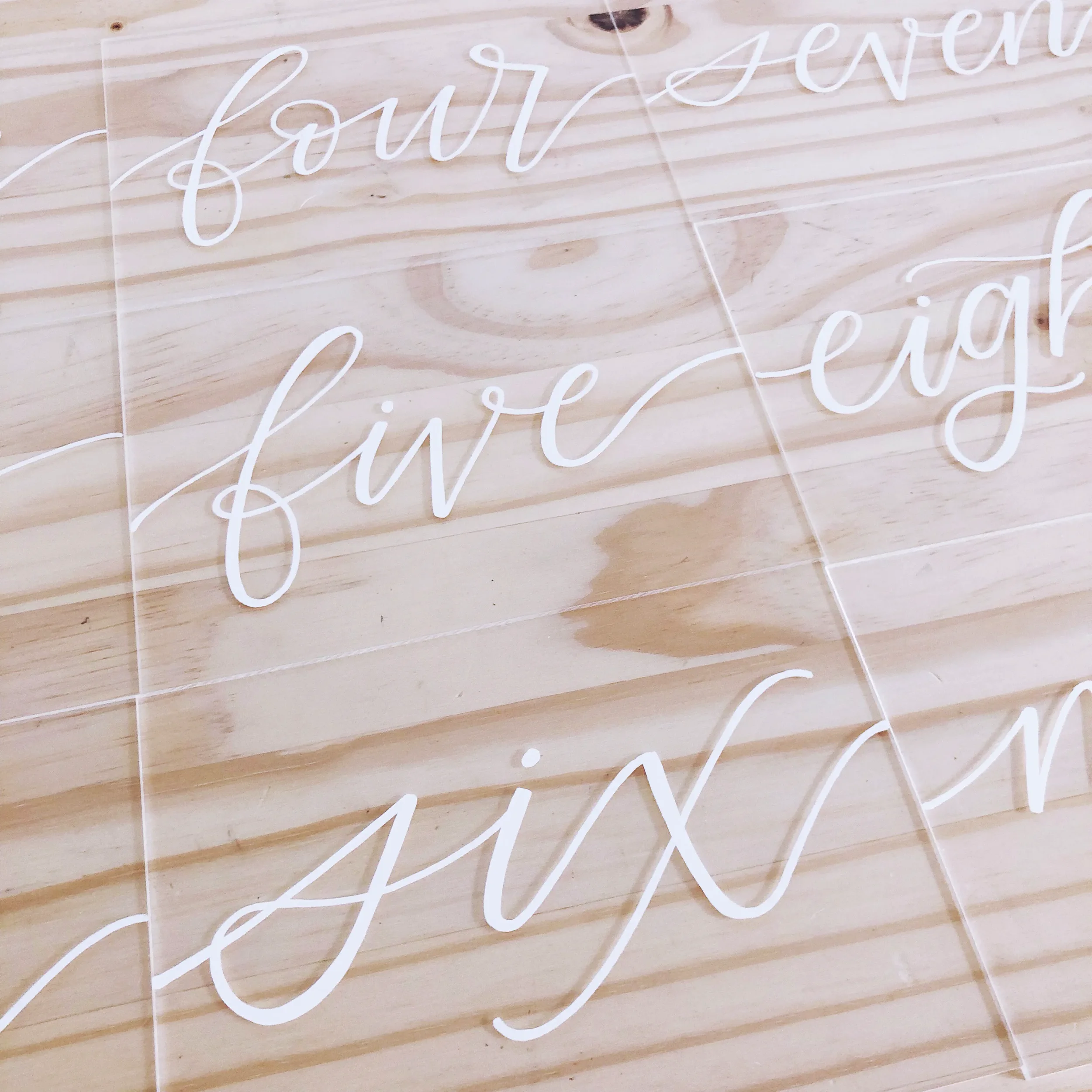 White calligraphy table numbers on clear acrylic.