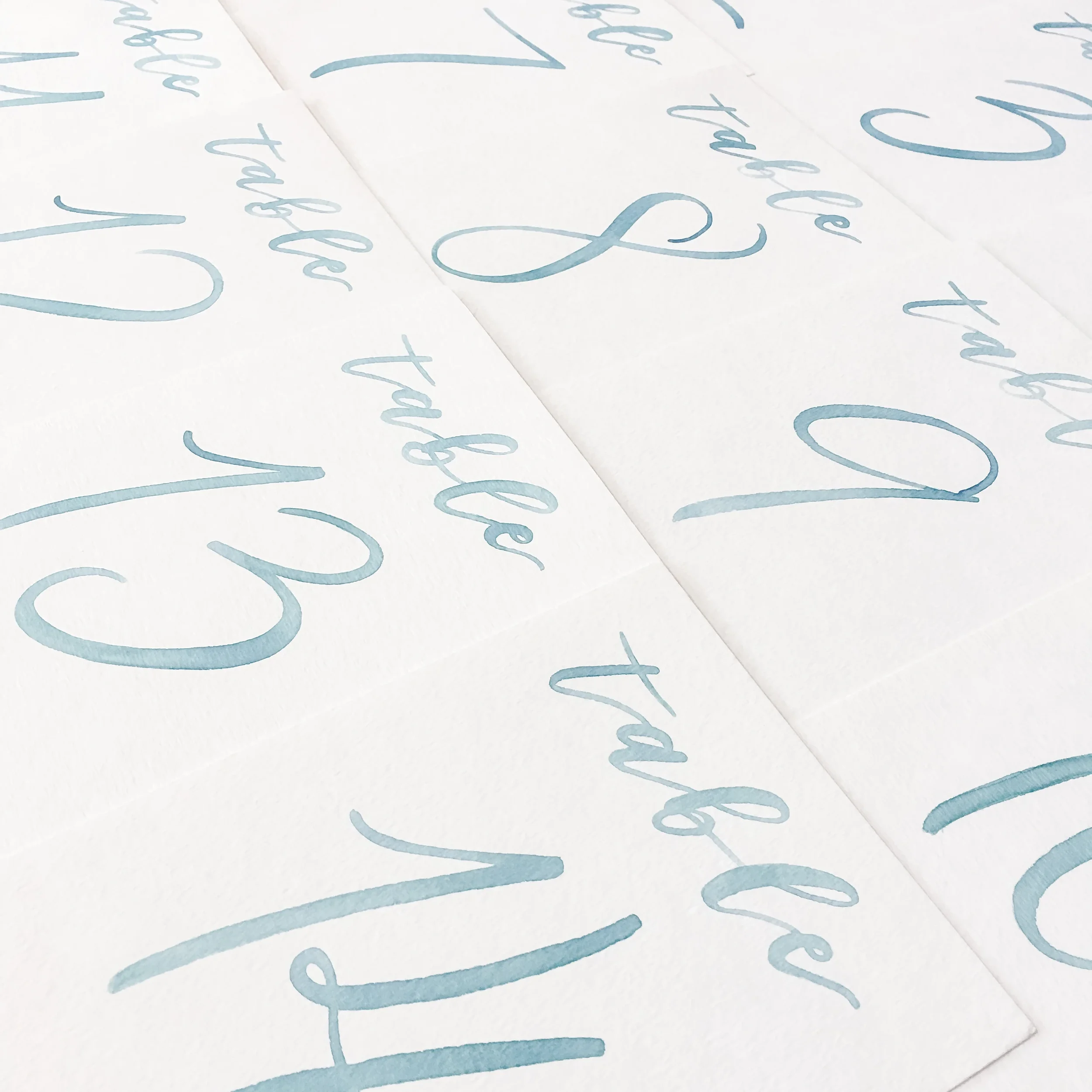 White paper reception table cards numbered two through fourteen in modern dusty blue ink.