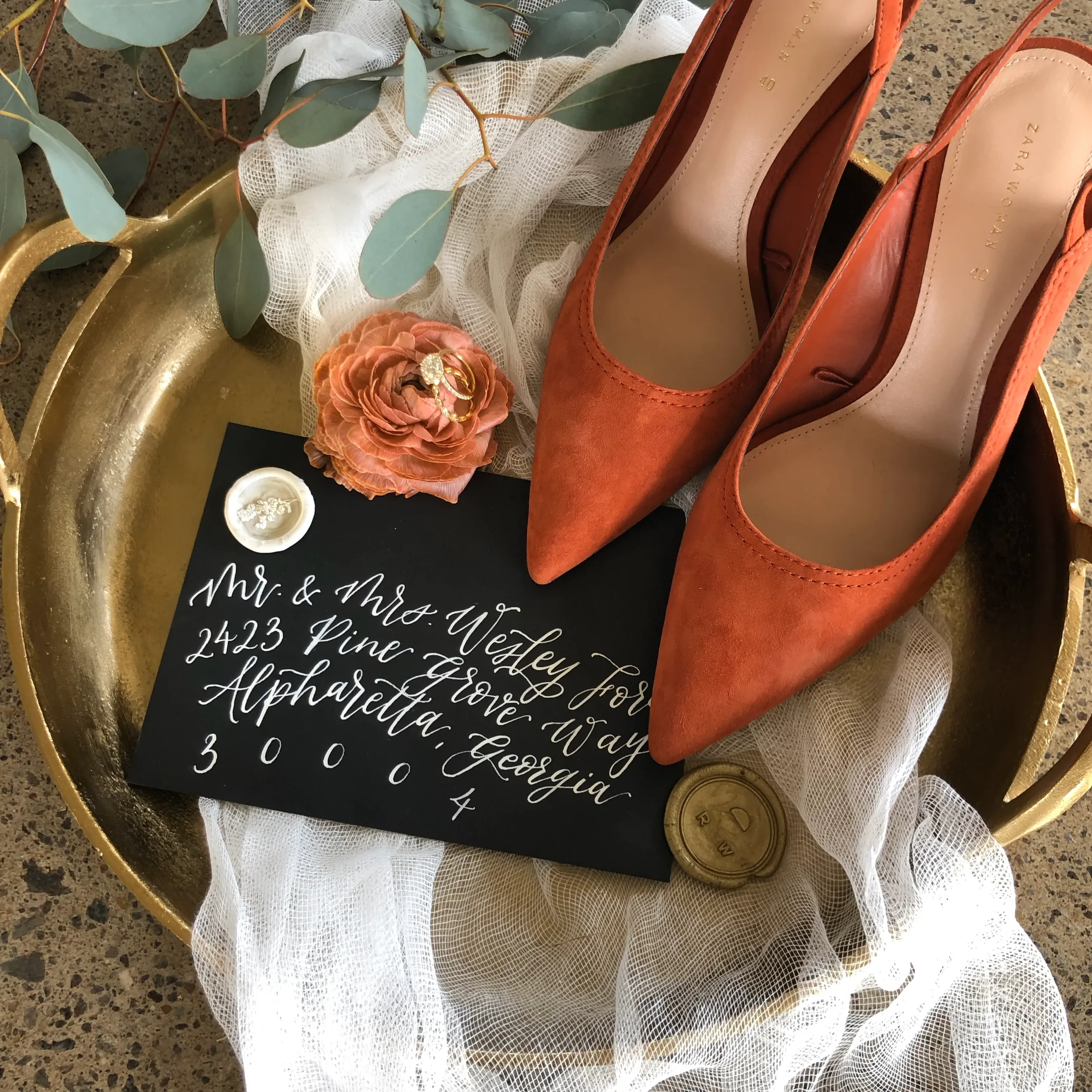 High-contrast wedding details flat lay with white ink script on black paper and fresh eucalyptus greenery.