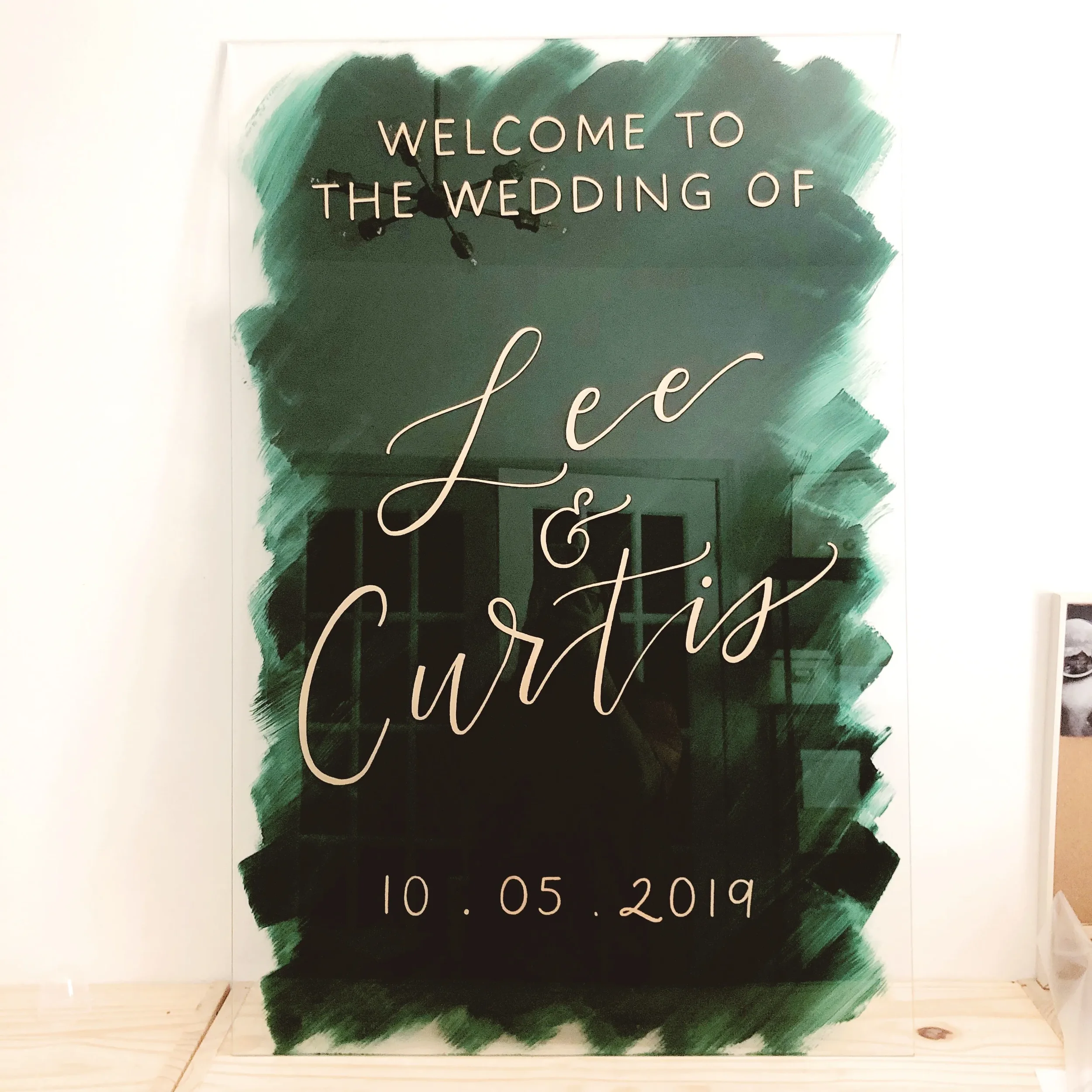 Emerald green painted-back acrylic wedding welcome sign featuring polished gold script calligraphy.
