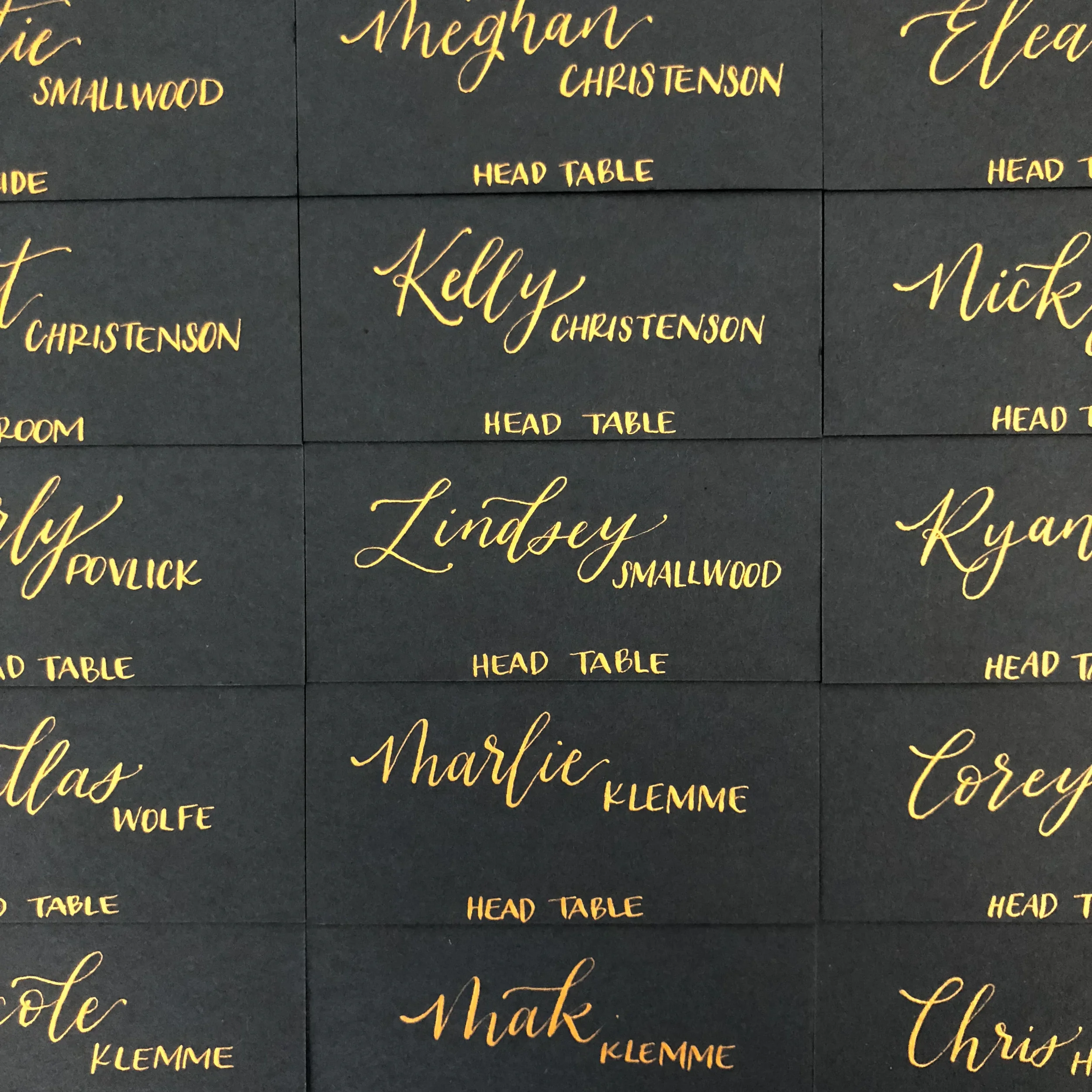 Array of matte black escort cards featuring elegant metallic gold calligraphy script for head table seating.