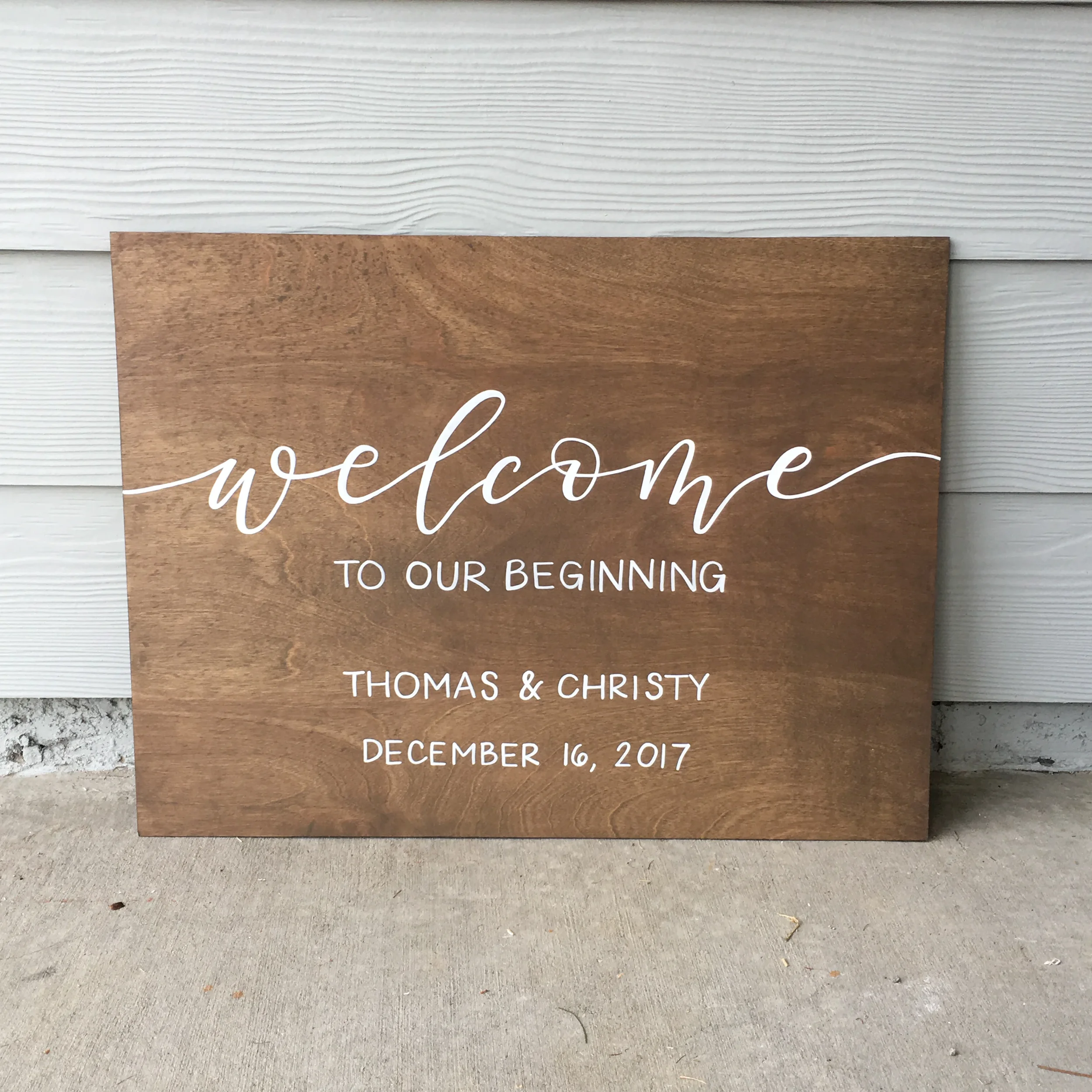 Rustic wooden welcome board featuring modern calligraphy script and event date displayed outdoors.