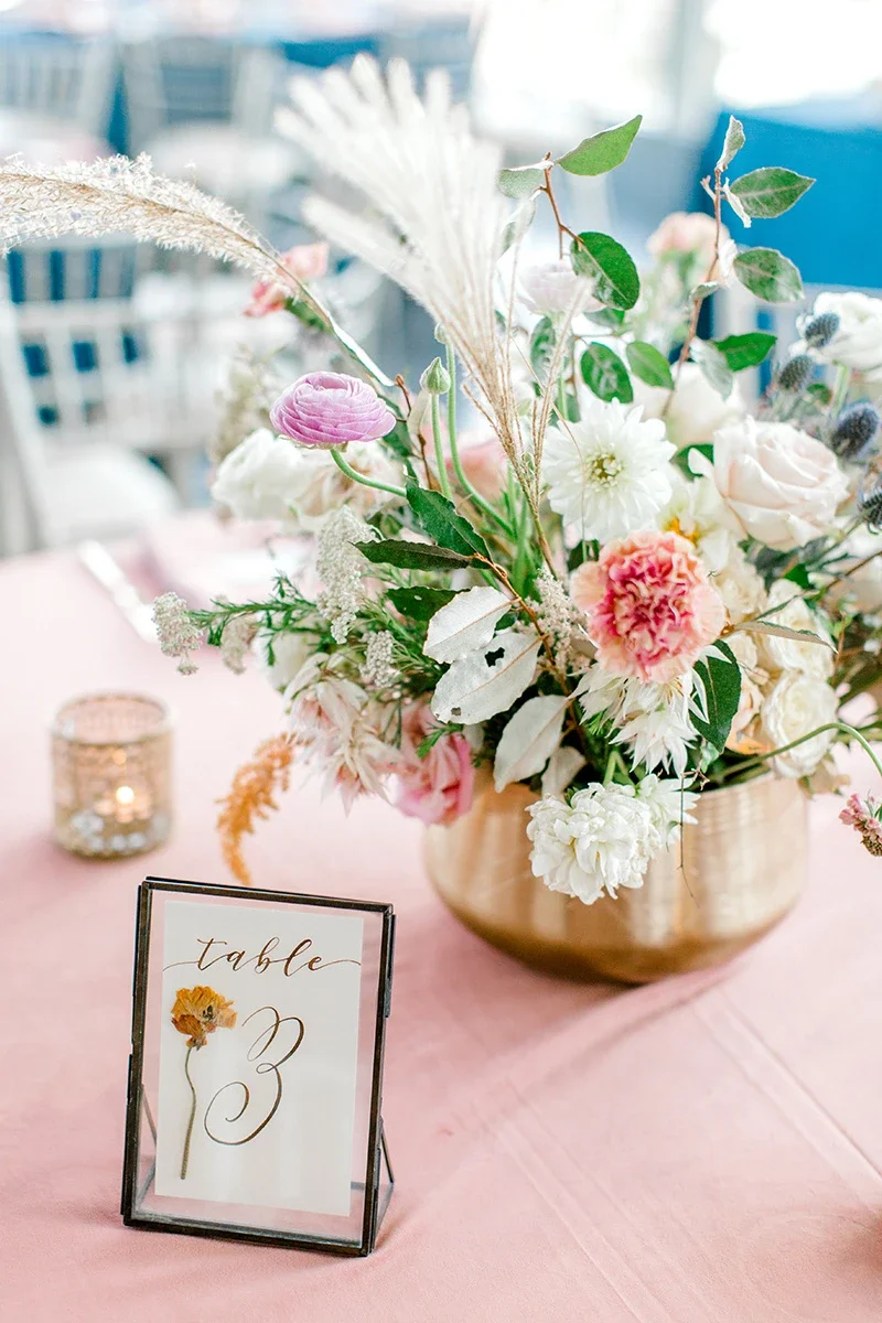 Romantic blush pink wedding table setting featuring a brass flower arrangement and custom glass table sign.