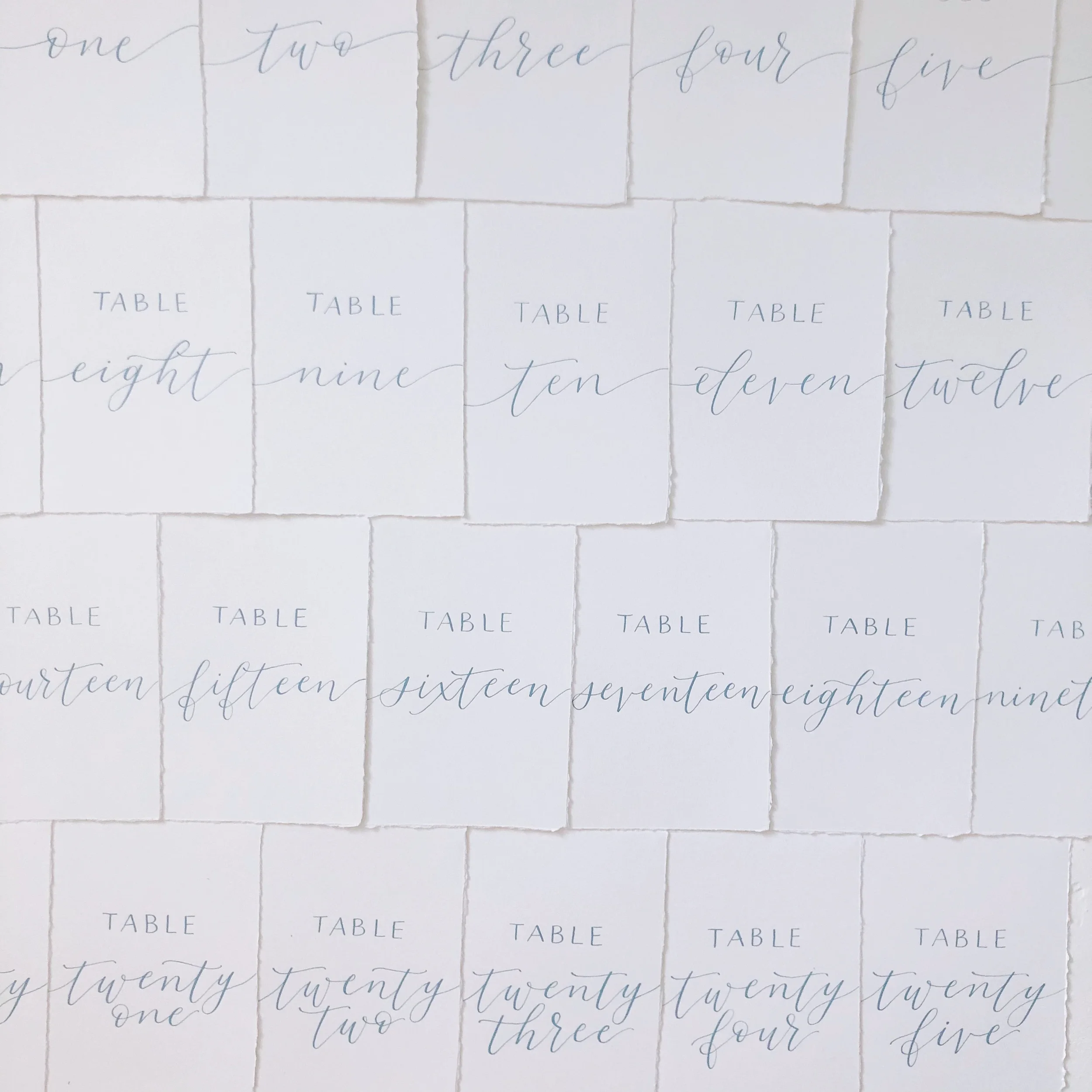 Dusty blue calligraphy ink table numbers on white cardstock with numbers written in script.