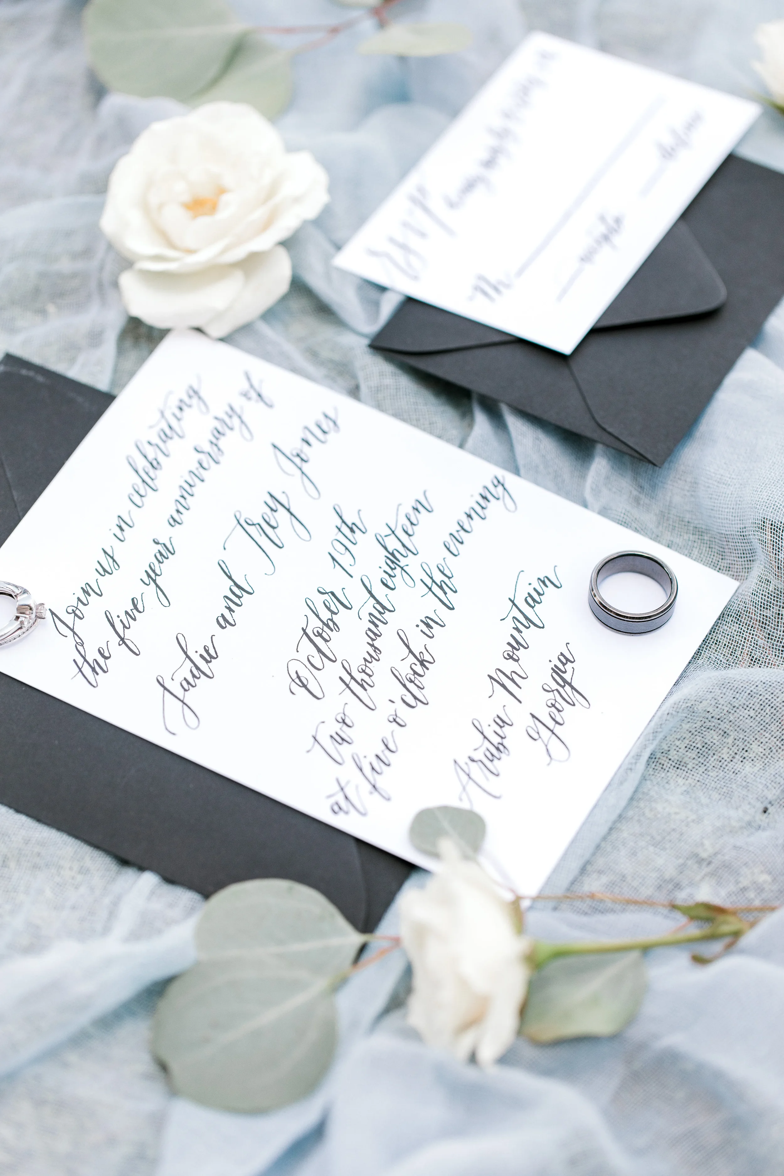 Classic black and white stationery design flat lay with custom cursive handwriting and accent greenery.