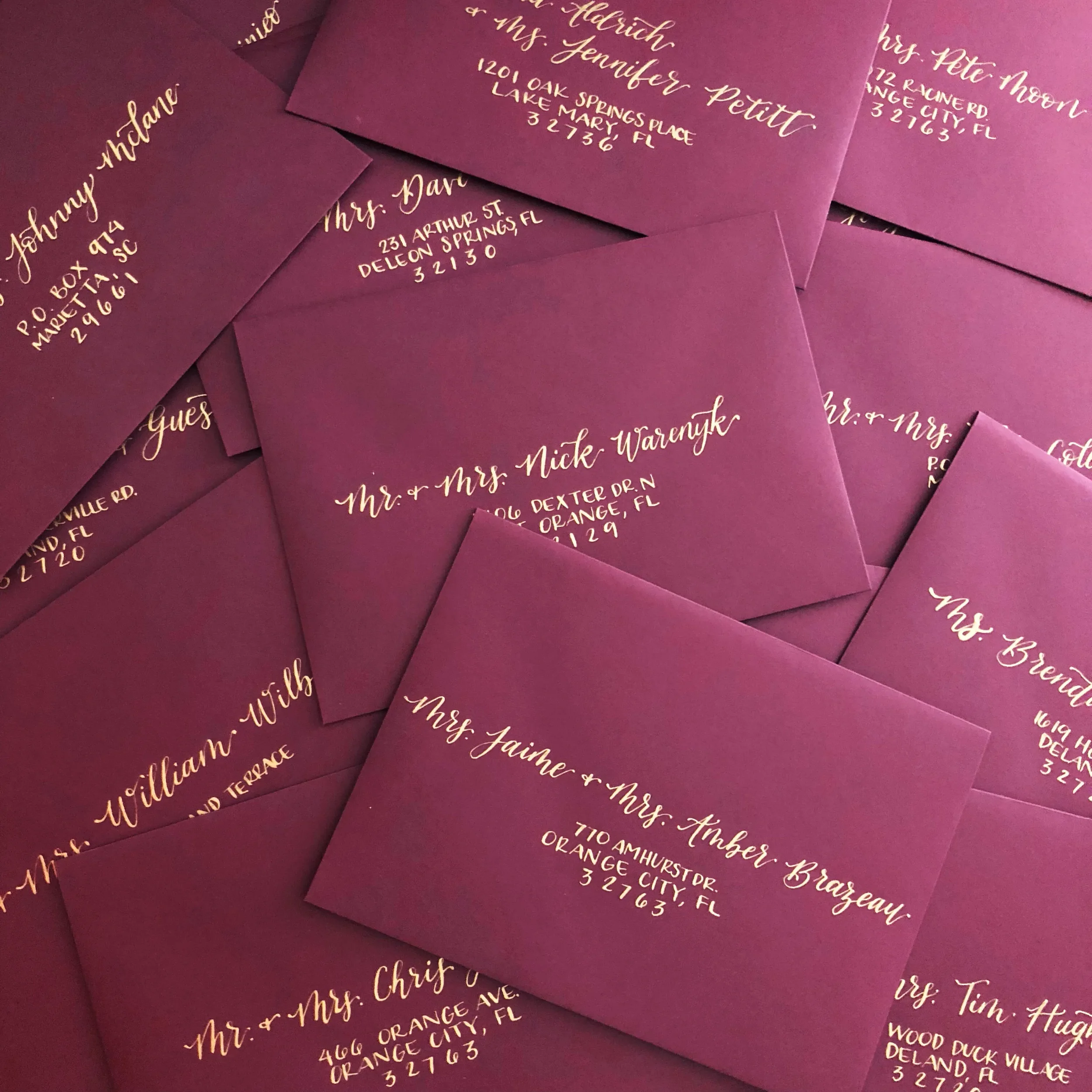 Stack of burgundy wedding envelopes addressed in metallic gold ink calligraphy script.