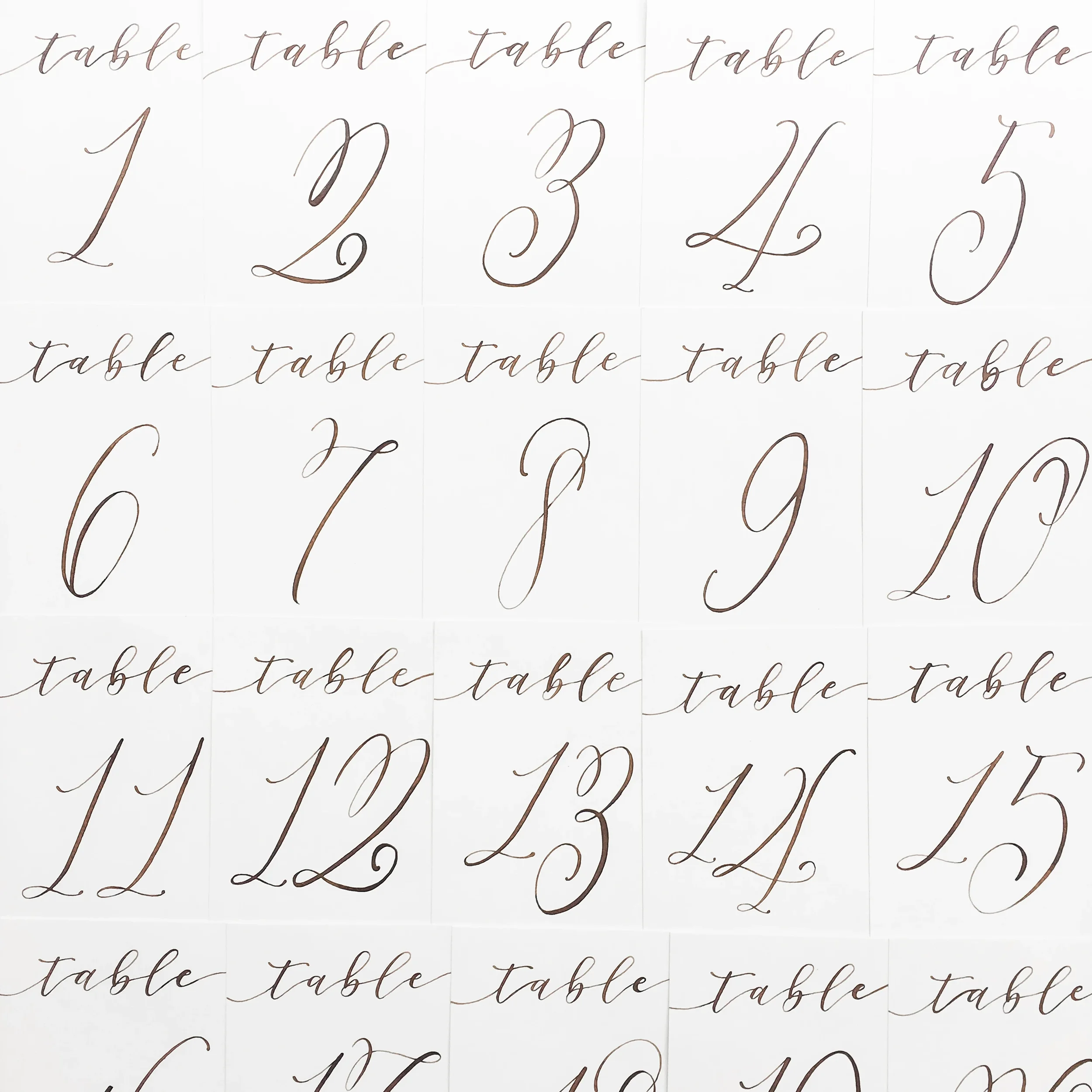Elegant calligraphed wedding table numbers printed on clean white paper in walnut brown calligraphy ink.