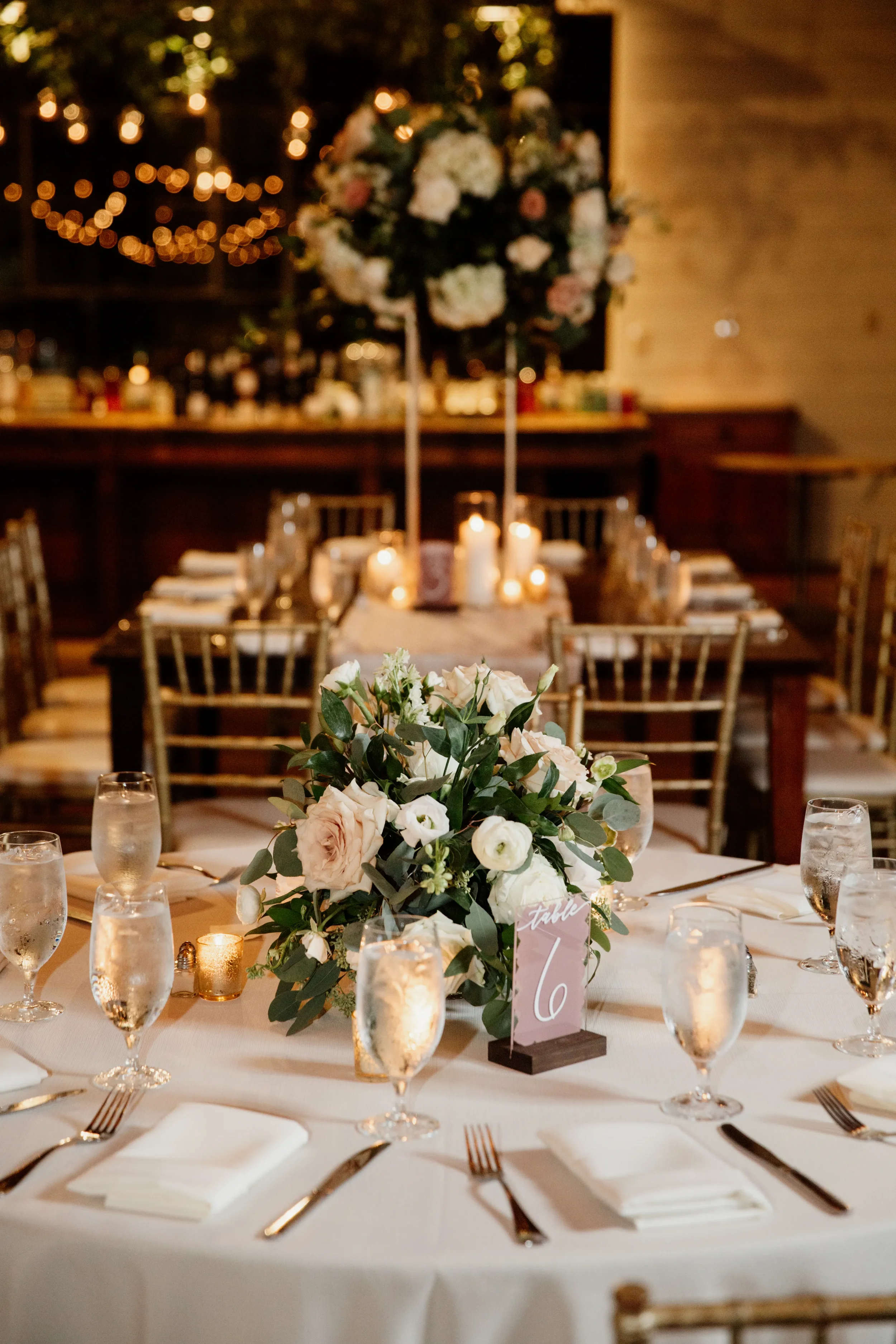Sophisticated custom acrylic table numbers featuring a rich, dusty mauve painted back and crisp white hand-lettered numbers, this signage design sits in a dark wooden block to beautifully complement romantic lush floral centerpieces and glowing candl
