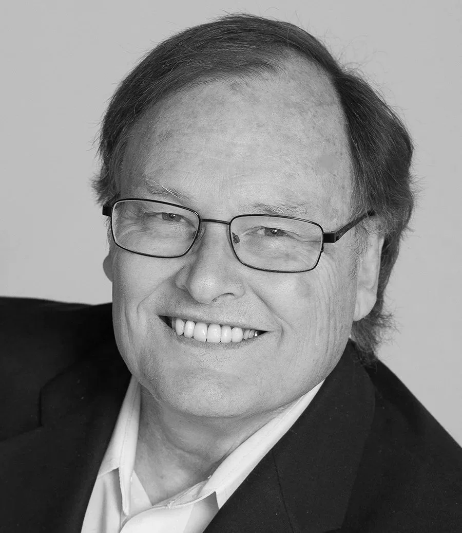 Black and white portrait of a smiling man with glasses, wearing a suit and white shirt.