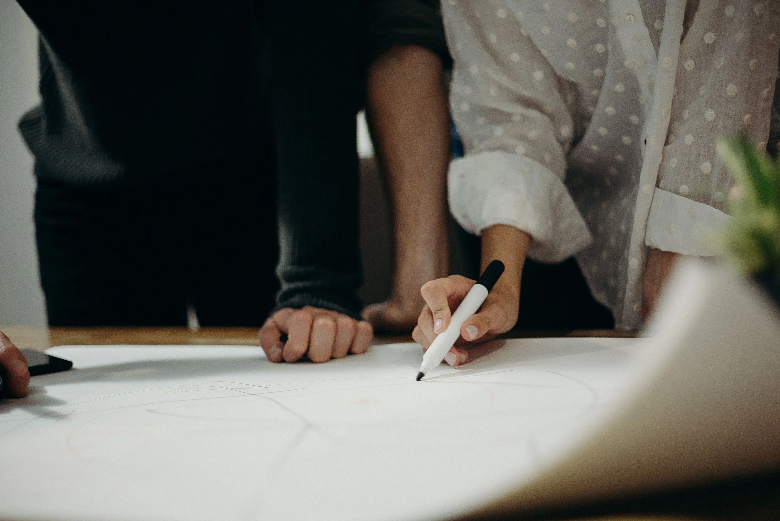 People gathered around a table writing on large sheets of paper with a black marker.