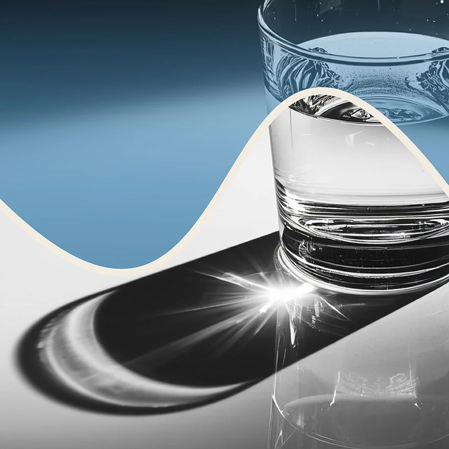 A clear glass of water with sunlight reflecting off the surface, casting a shadow on the table.