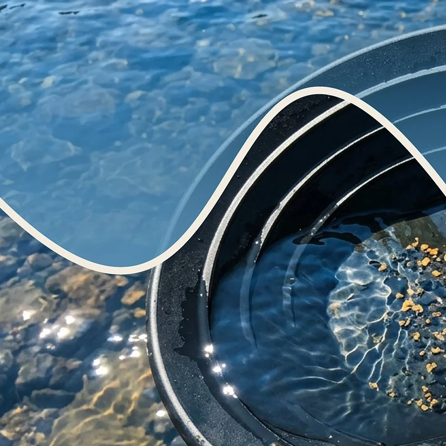 Close-up of a black bucket filled with water and some small floating debris, resting on a gravel surface near a body of water.