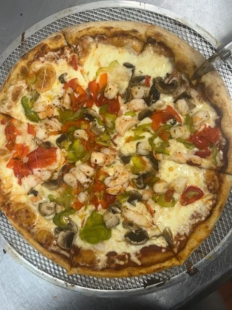 Cheese pizza topped with shrimp, black olives, green peppers, and red peppers served on a wire rack.