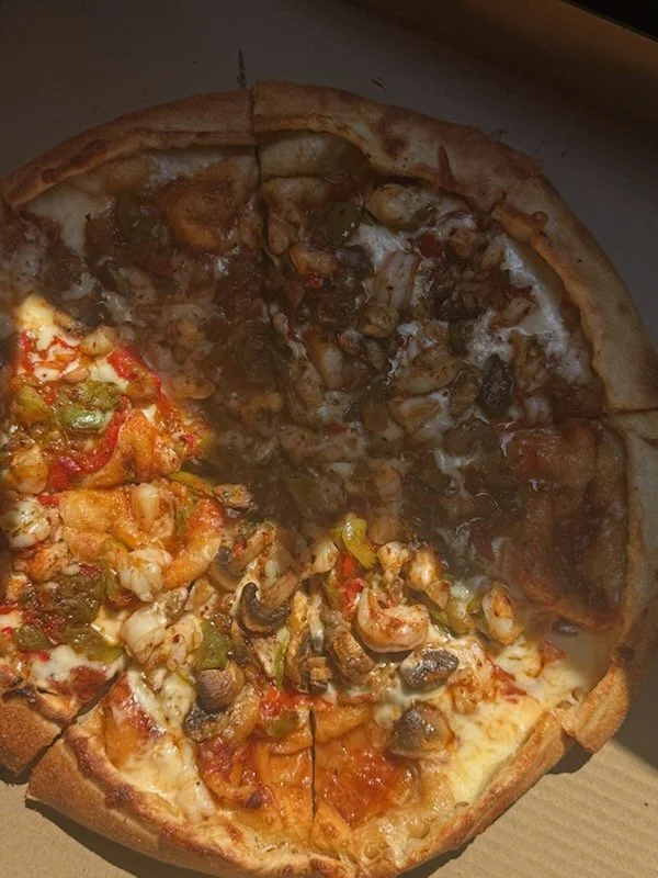 A pizza with four different sections topped with different ingredients such as shrimp, vegetables, mushrooms, and beef.