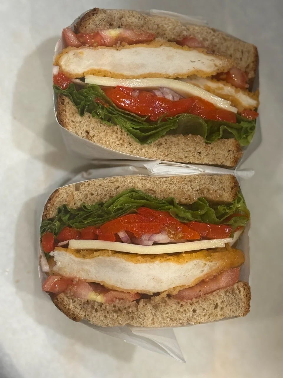 Two breakfast sandwiches with egg, bacon, cheese, lettuce, tomato, and bread.