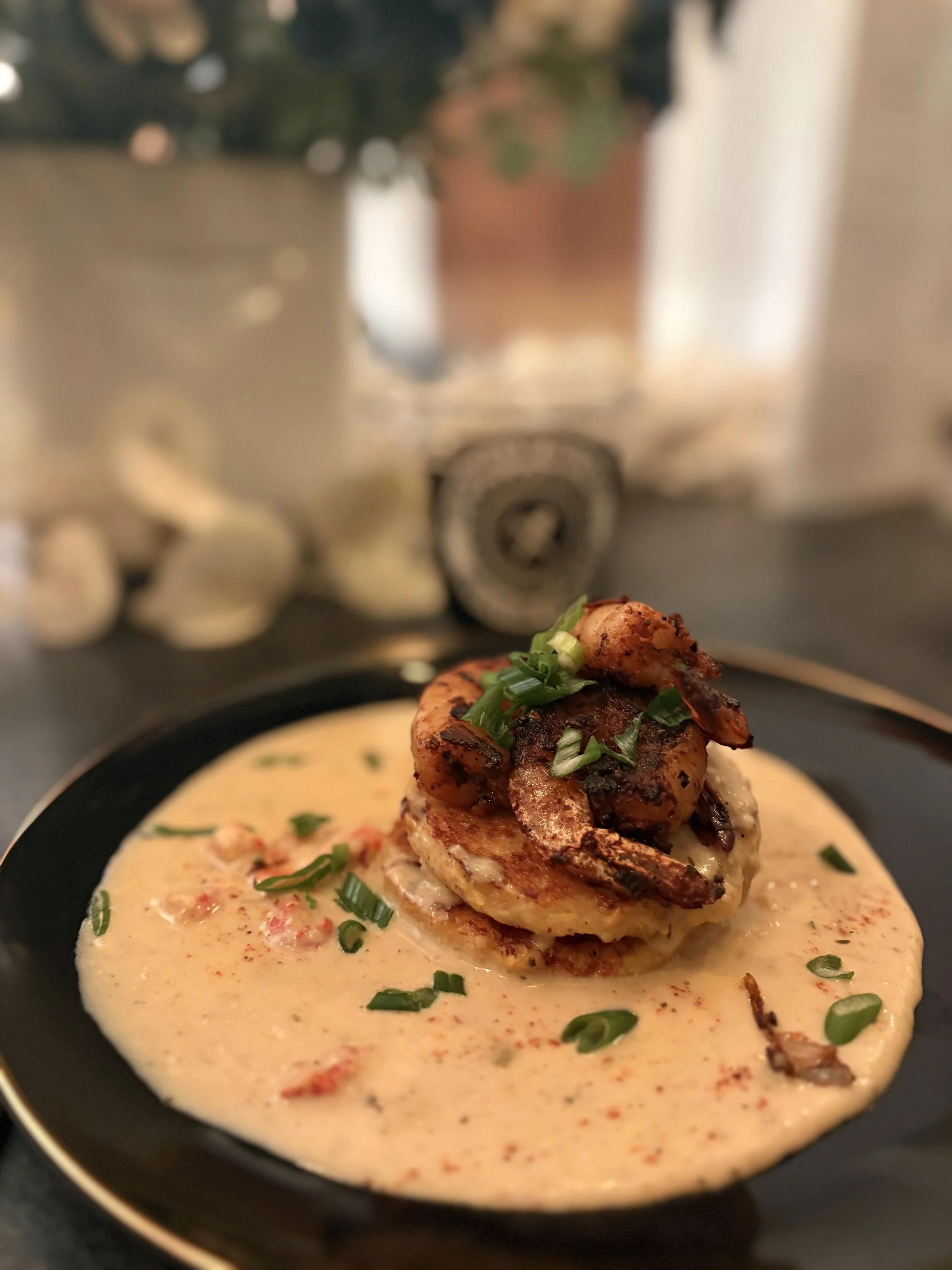 Close-up of a seafood dish with a grilled lobster tail and chopped green onions on top, served in a creamy sauce in a black bowl.