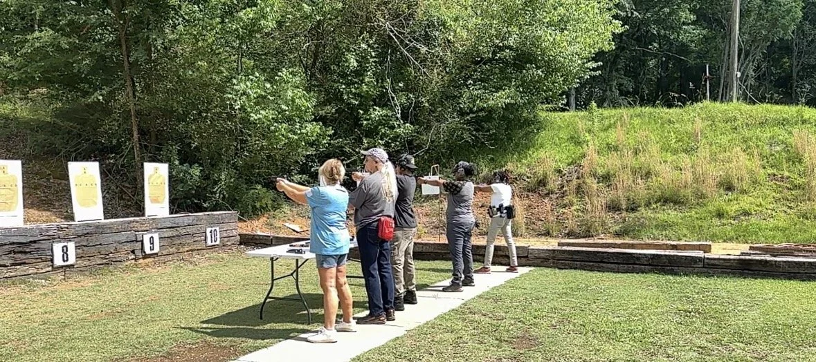 People participating in a shooting range practice outdoors, aiming firearms at targets.