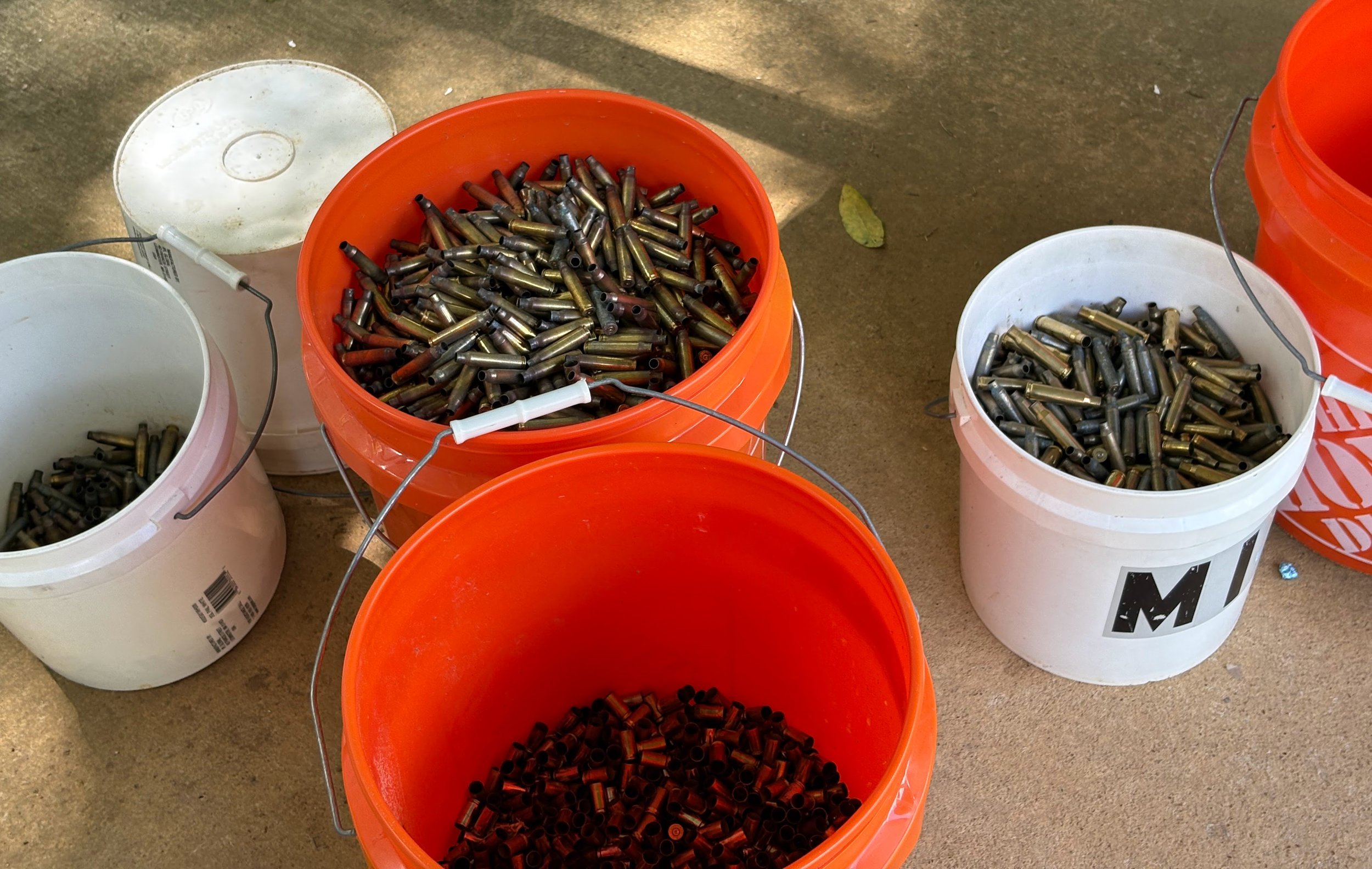 Multiple paint buckets filled with spent shell casings on a concrete floor.