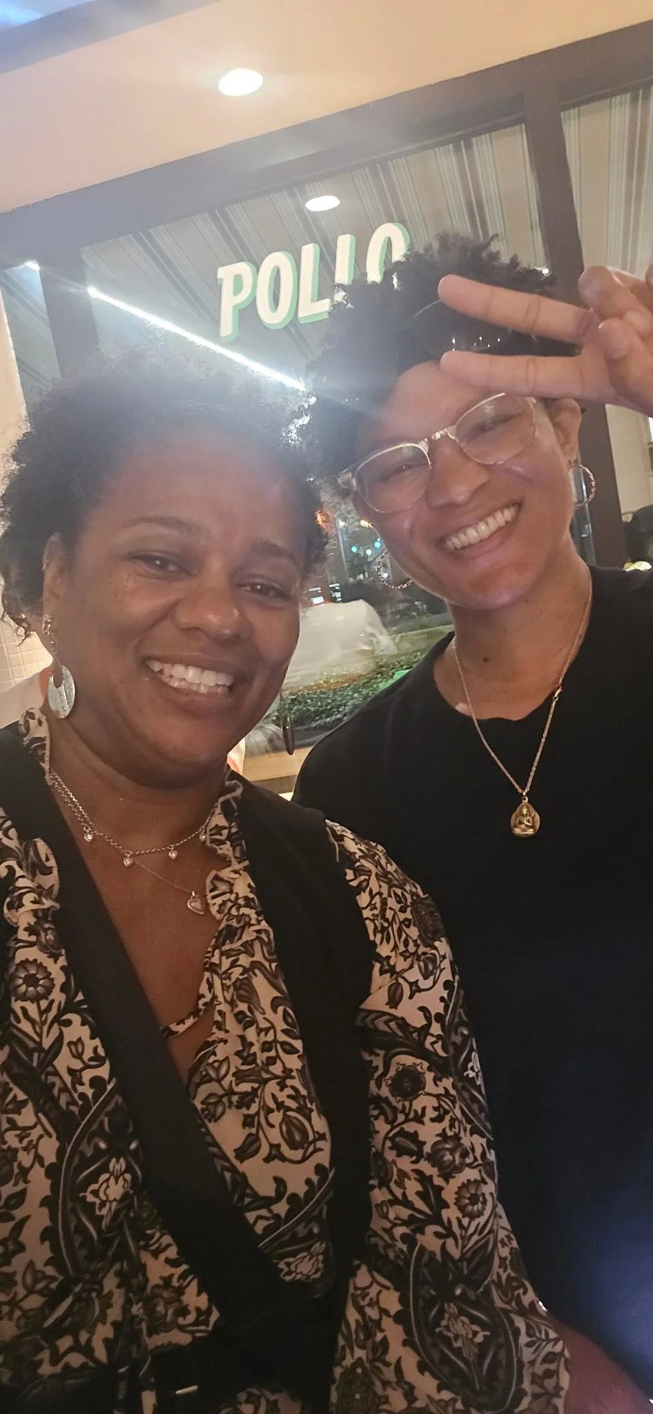 Two women smiling for a selfie in front of a POLLO restaurant at night.