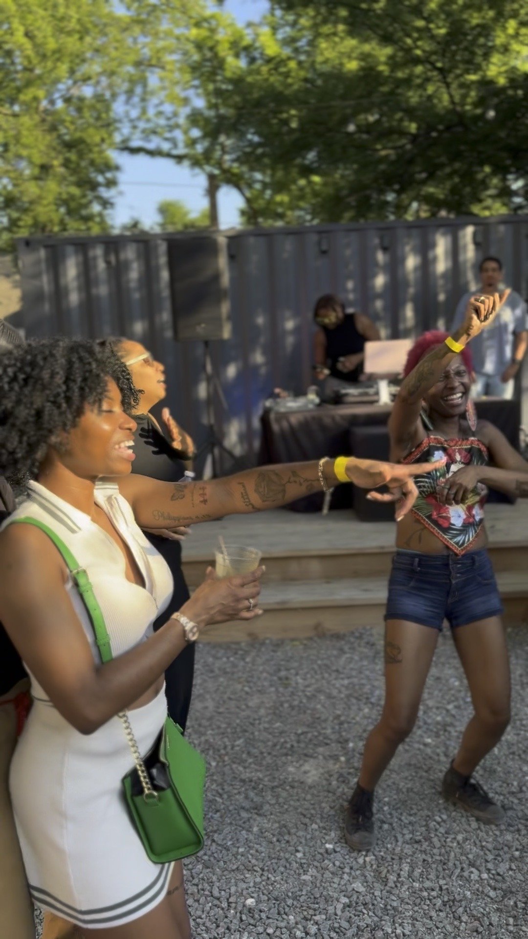 Two women dancing outdoors at a social event, with a woman holding a drink in her hand.