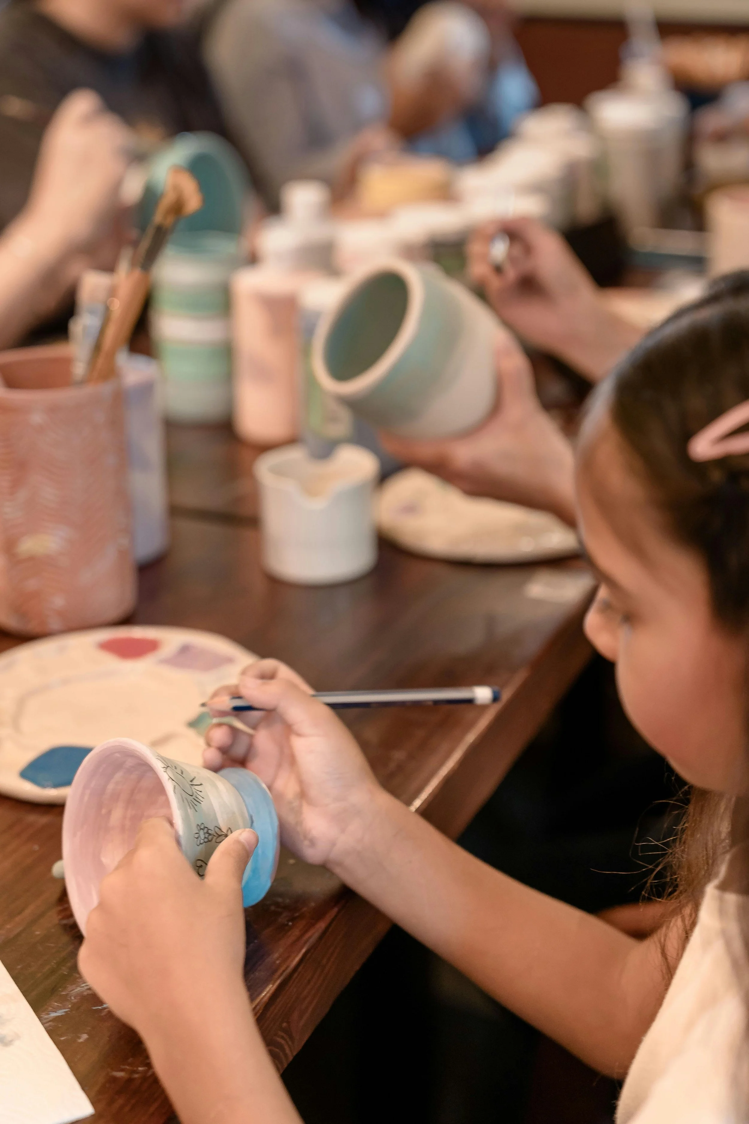 Children painting ceramic mugs at a wooden table.