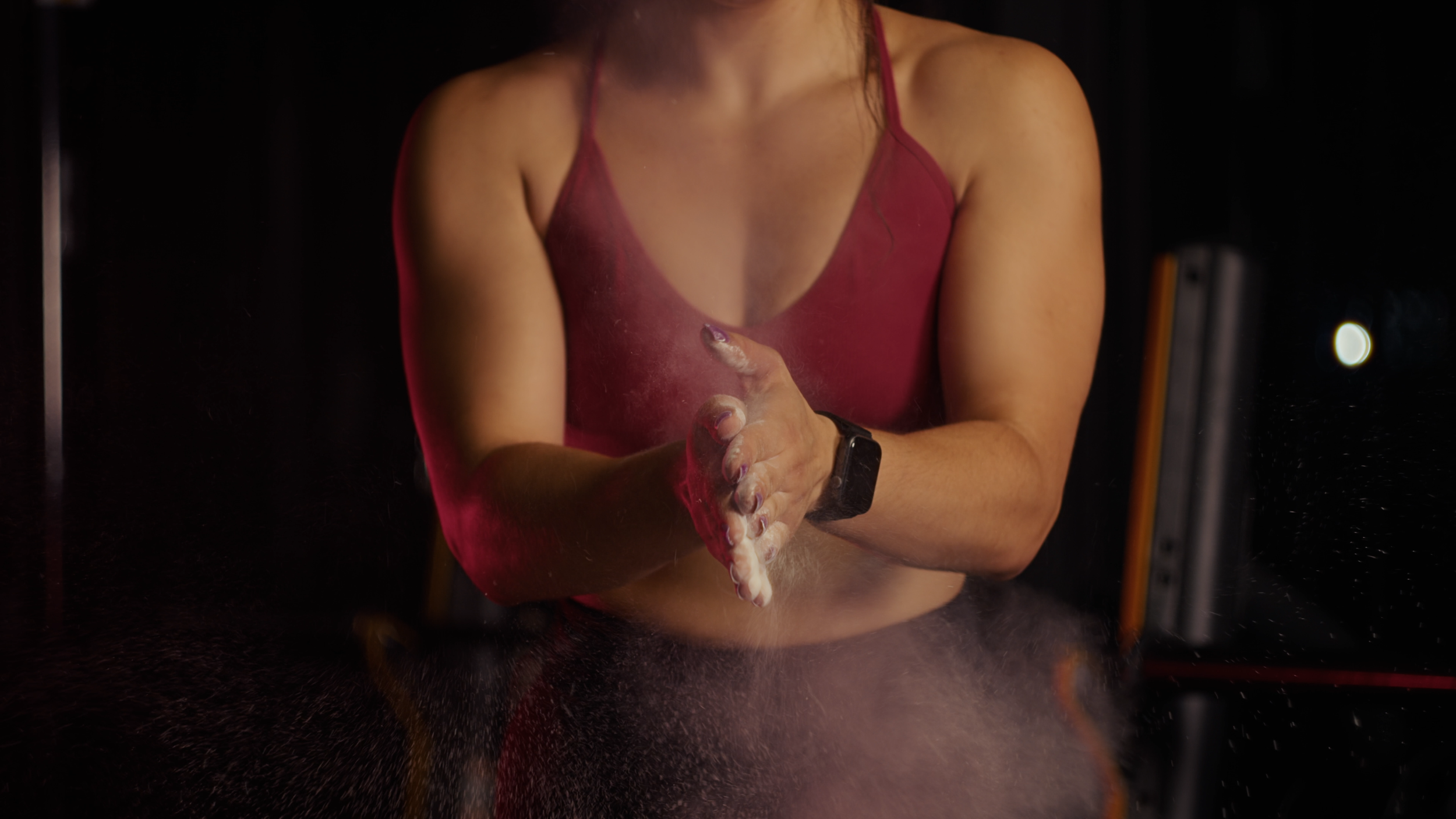 A woman in a pink tank top washing her hands in a sink with water and soap, looking at a mirror with her reflection visible.