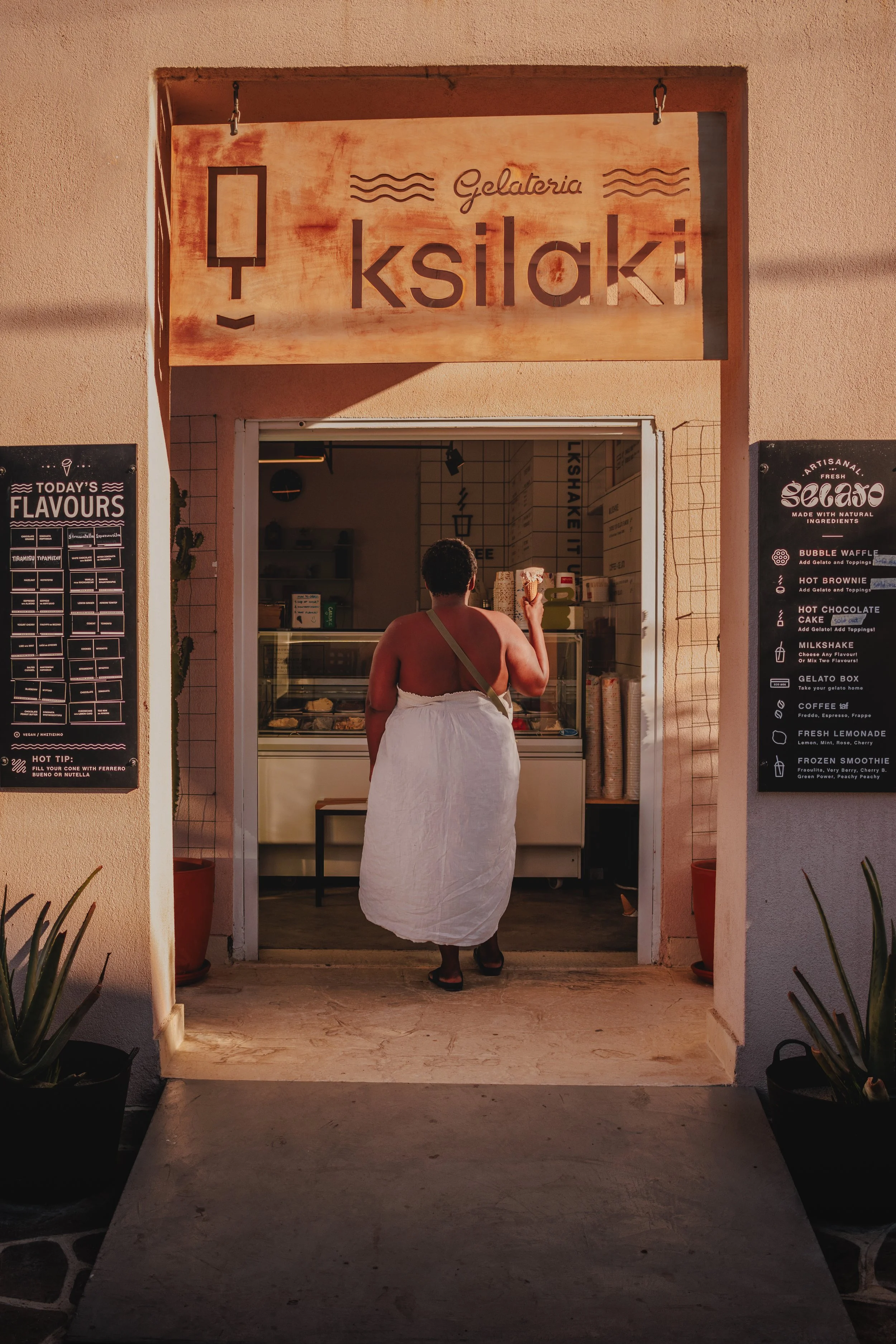 A person wearing a white towel or dress, with dark hair, standing inside an ice cream shop, facing the display case.