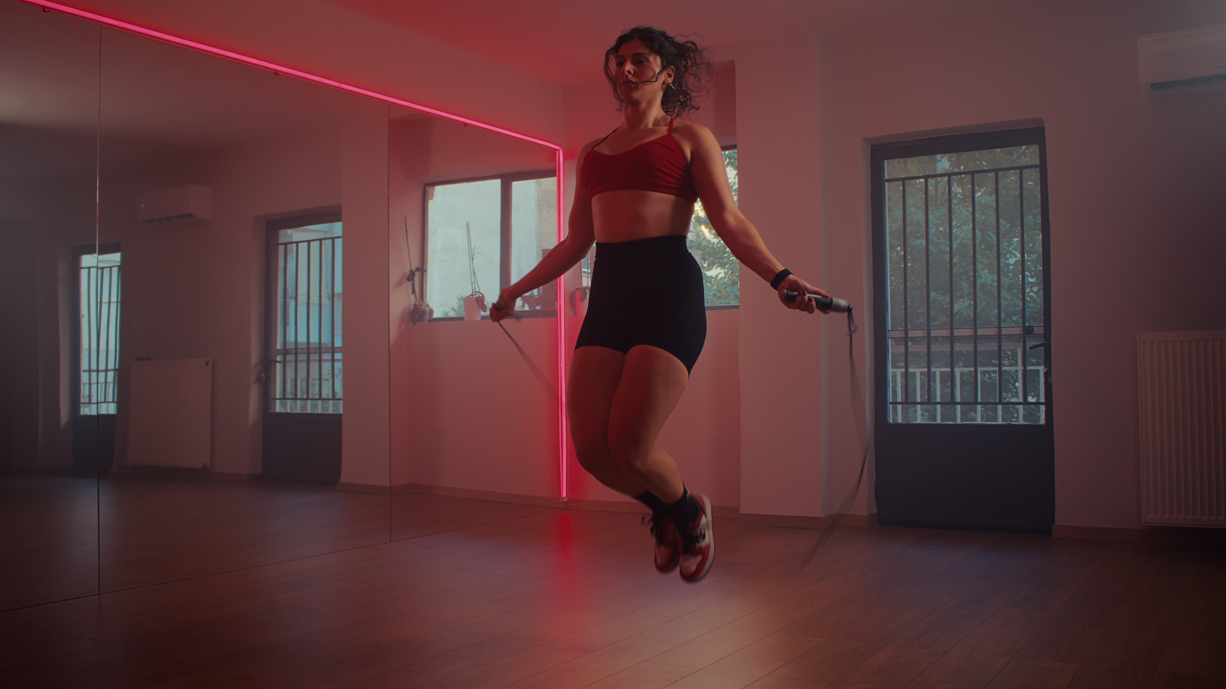Woman skipping rope during workout in a fitness studio with pink neon light and mirror walls.
