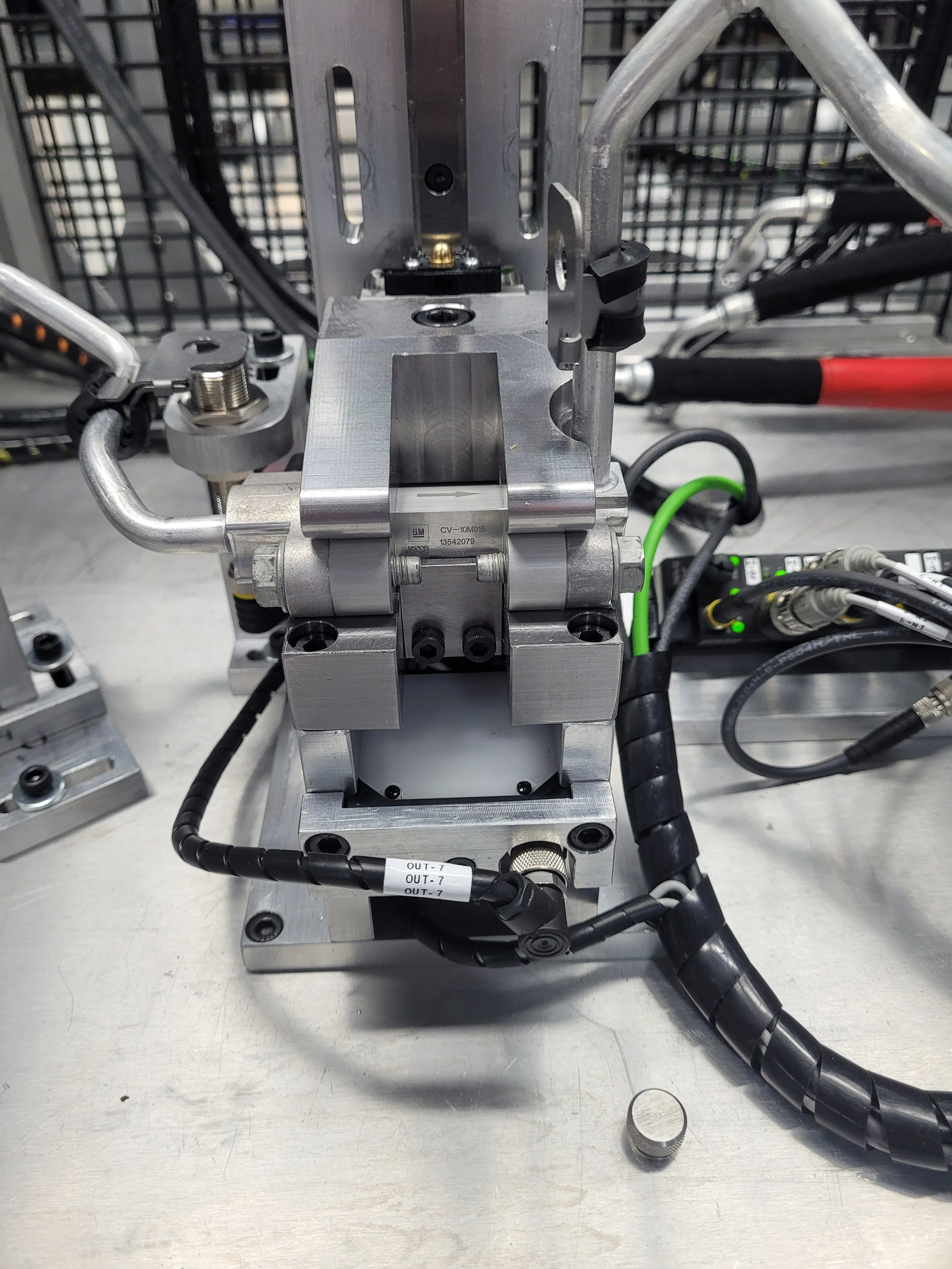 Close-up of an industrial mechanical device with metallic components, black and green cables, and several small screws, on a metallic work surface.