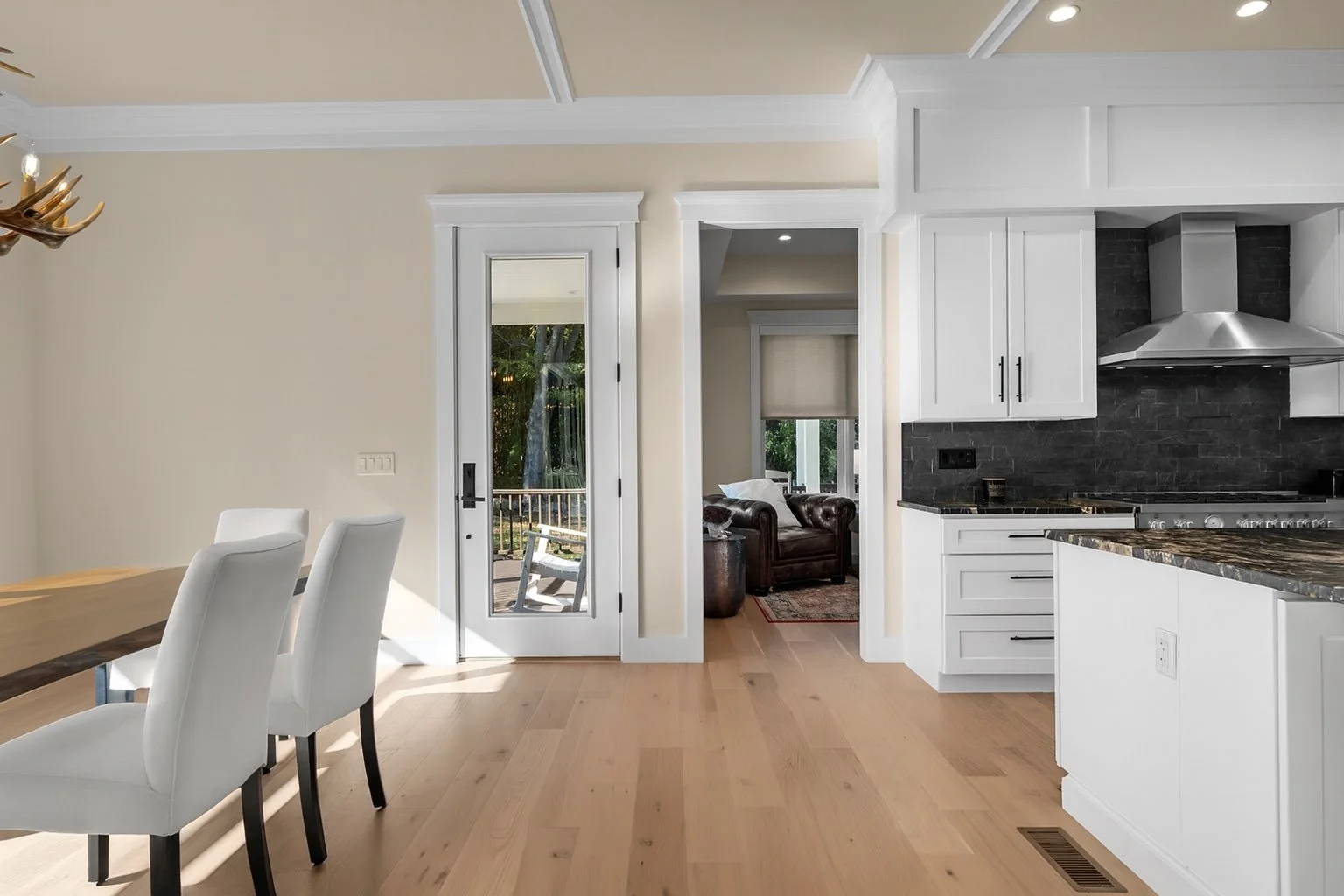 Bright, modern kitchen and dining area with white cabinets, black granite countertops, stainless steel range hood, and wooden flooring.