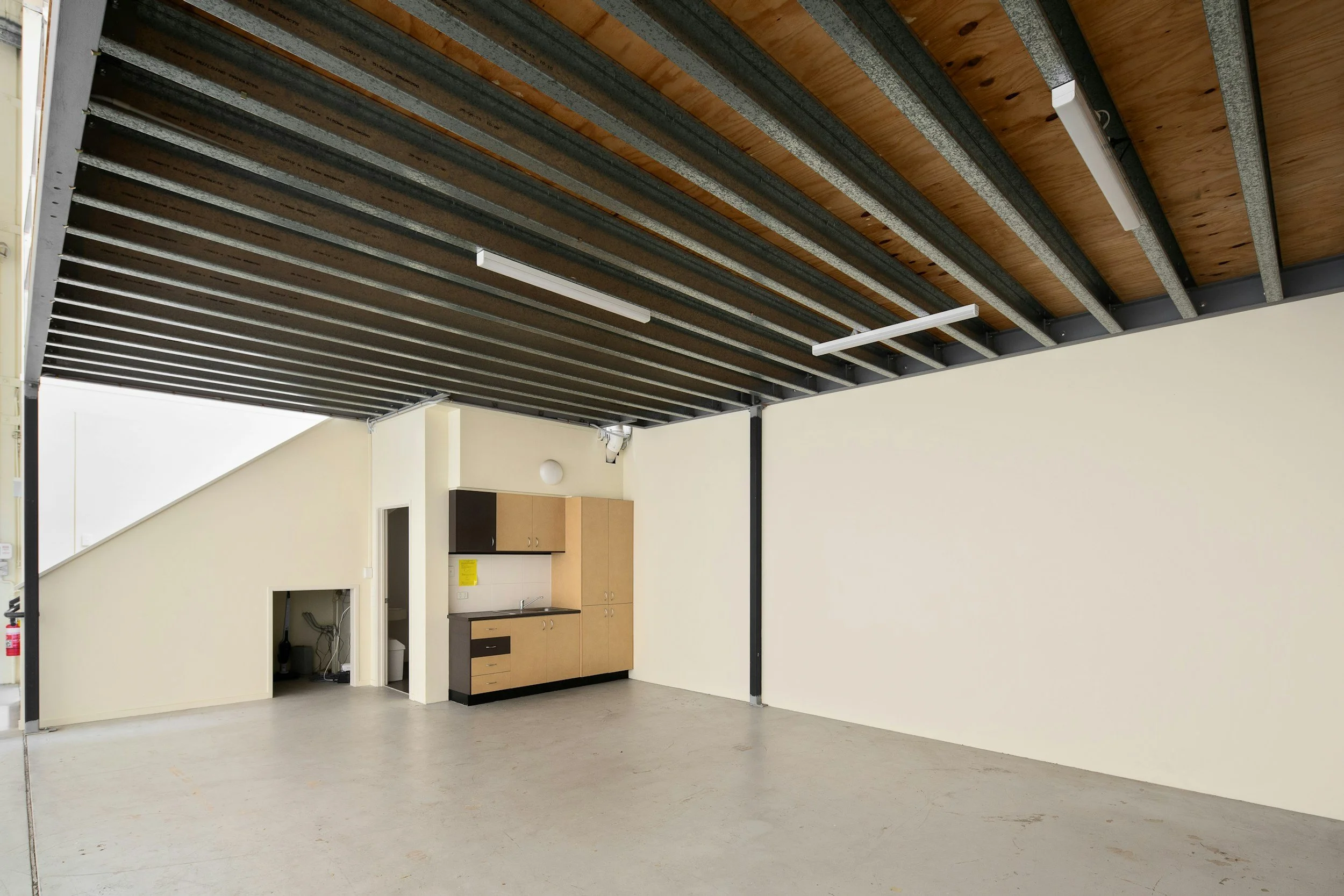 Empty room with a dropped ceiling, fluorescent lights, kitchen cabinets, and a small kitchenette area.