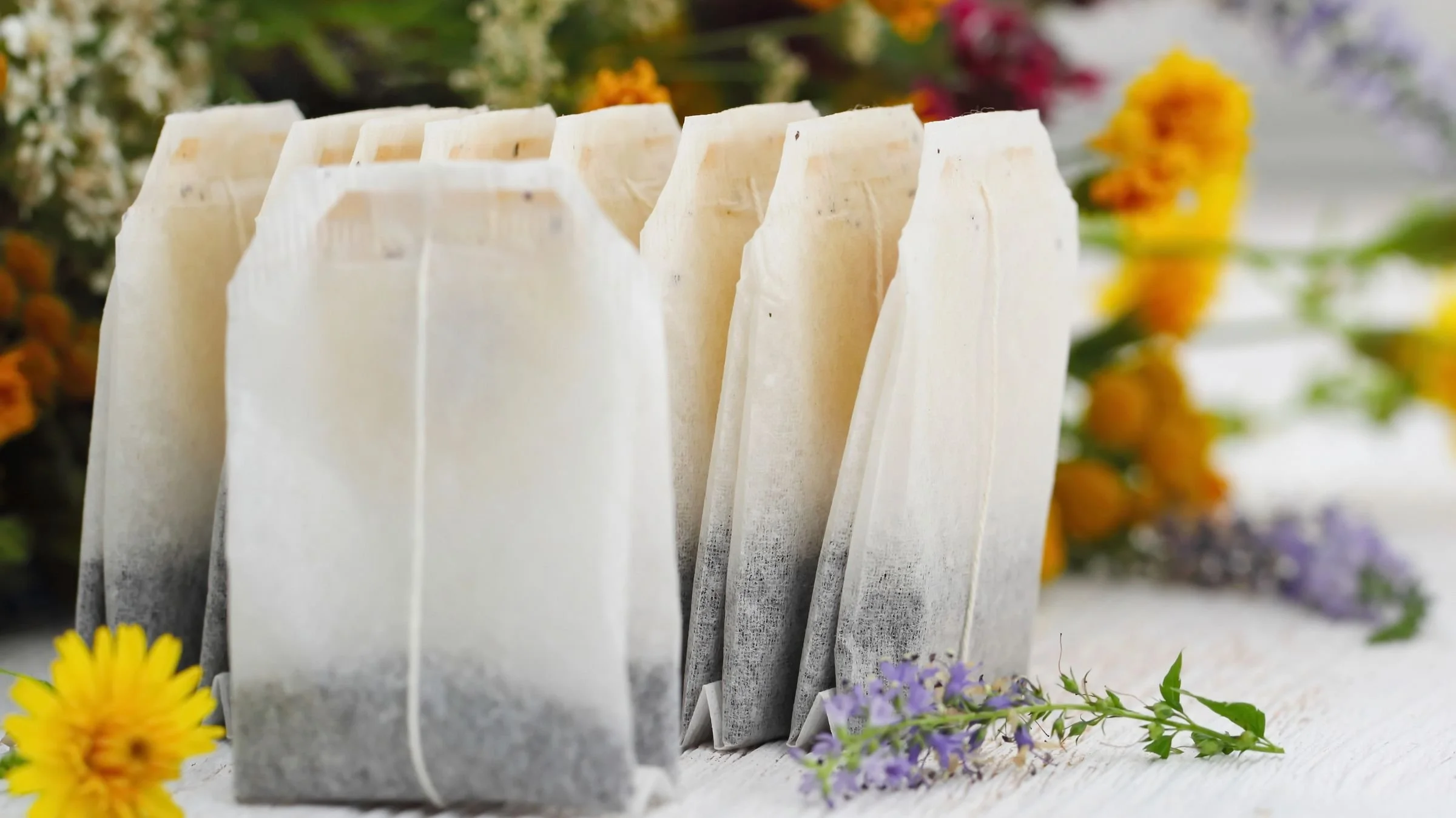 A row of white paper tickets or tags tied with string, with blurred colorful flowers in the background and foreground.